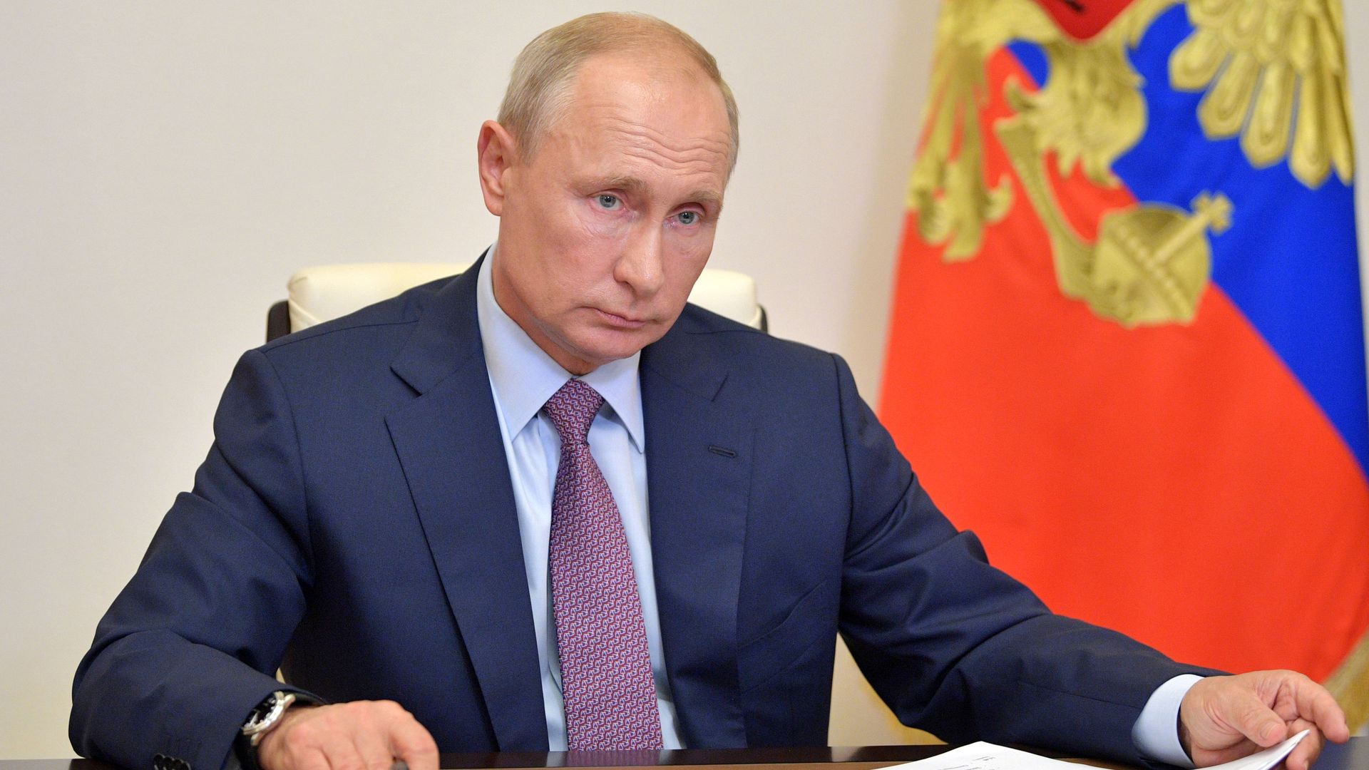 Vladimir Putin sits behind a desk holding papers