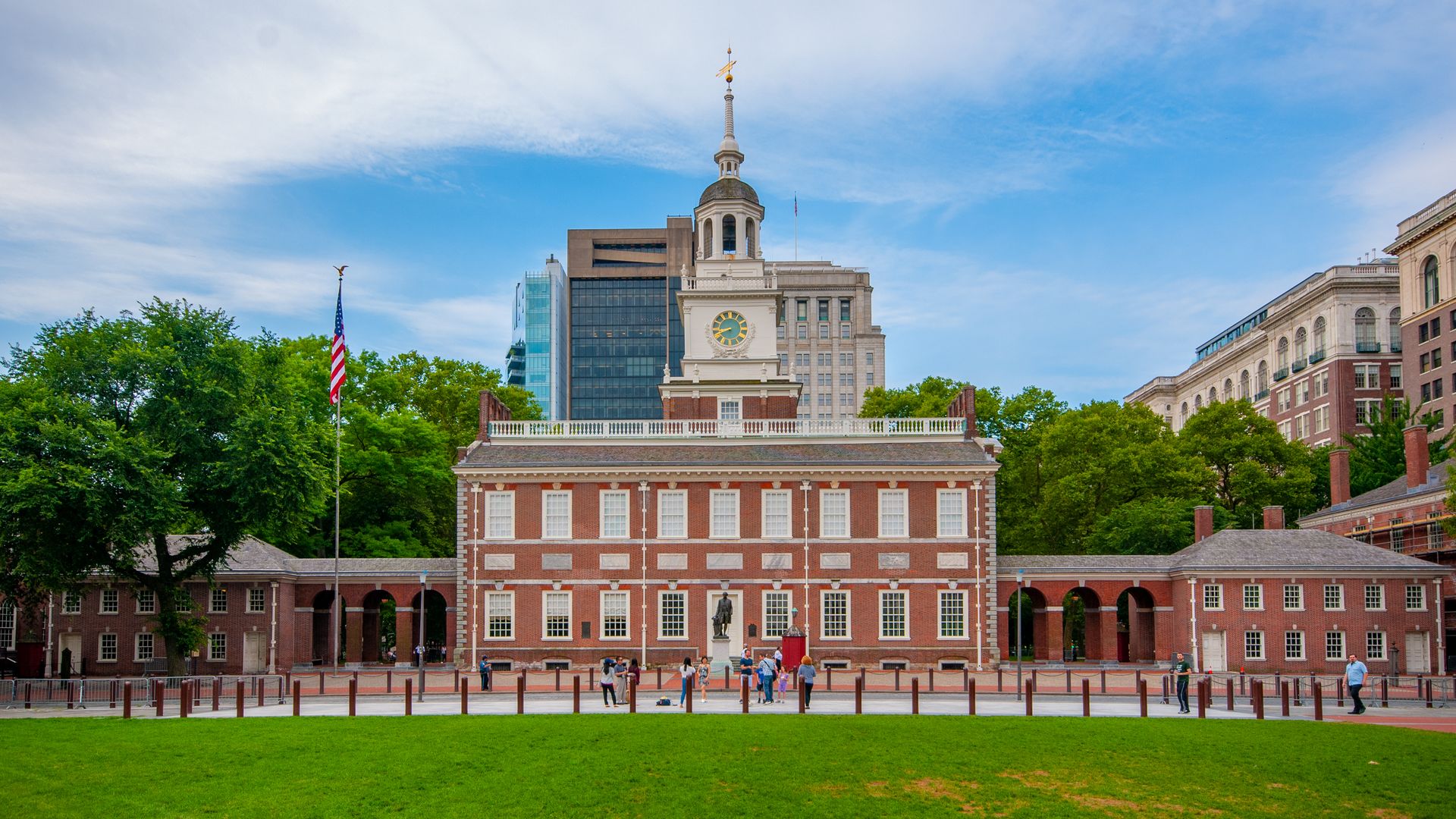 A stately, brick building with a clock tower with dozens of windows situated among a grassy lawn, blue skies and other buildings.