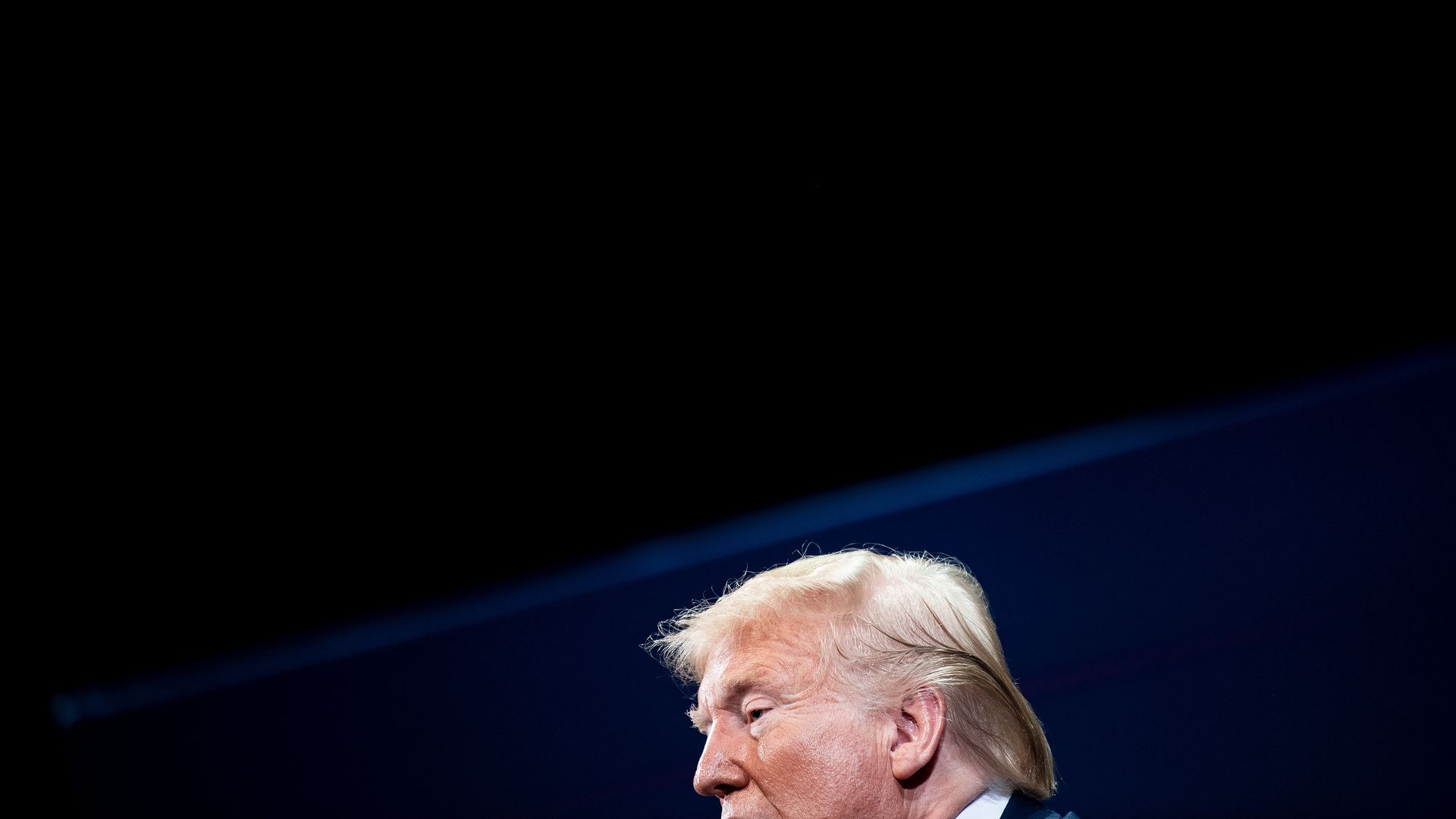 In this image, the top of Trump's head is visible against a dark background
