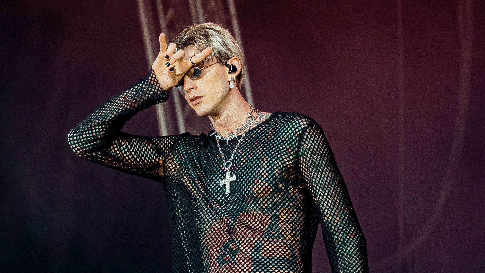 Machine Gun Kelly makes devil horns with his fingers on stage. 