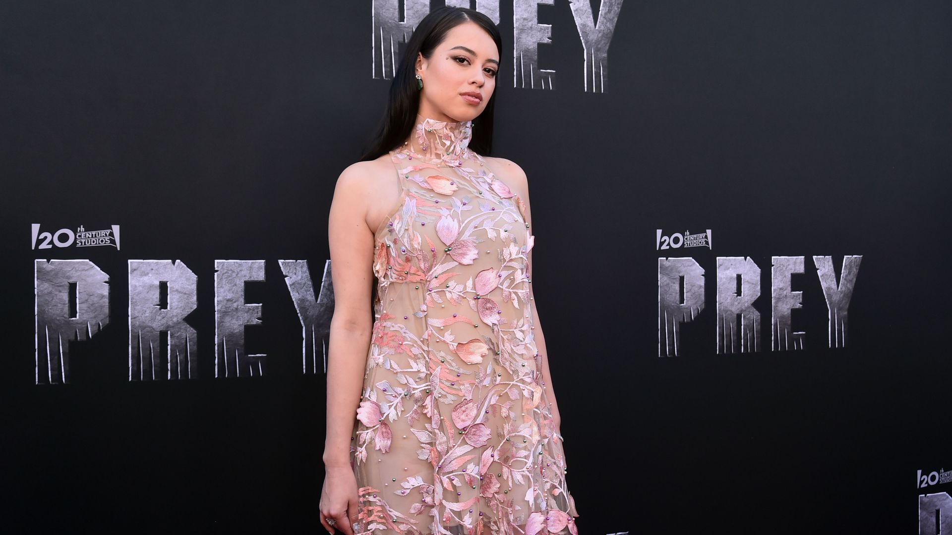 woman in a pink dress with flowers on it in front of a screen printed with Prey and 20th century fox