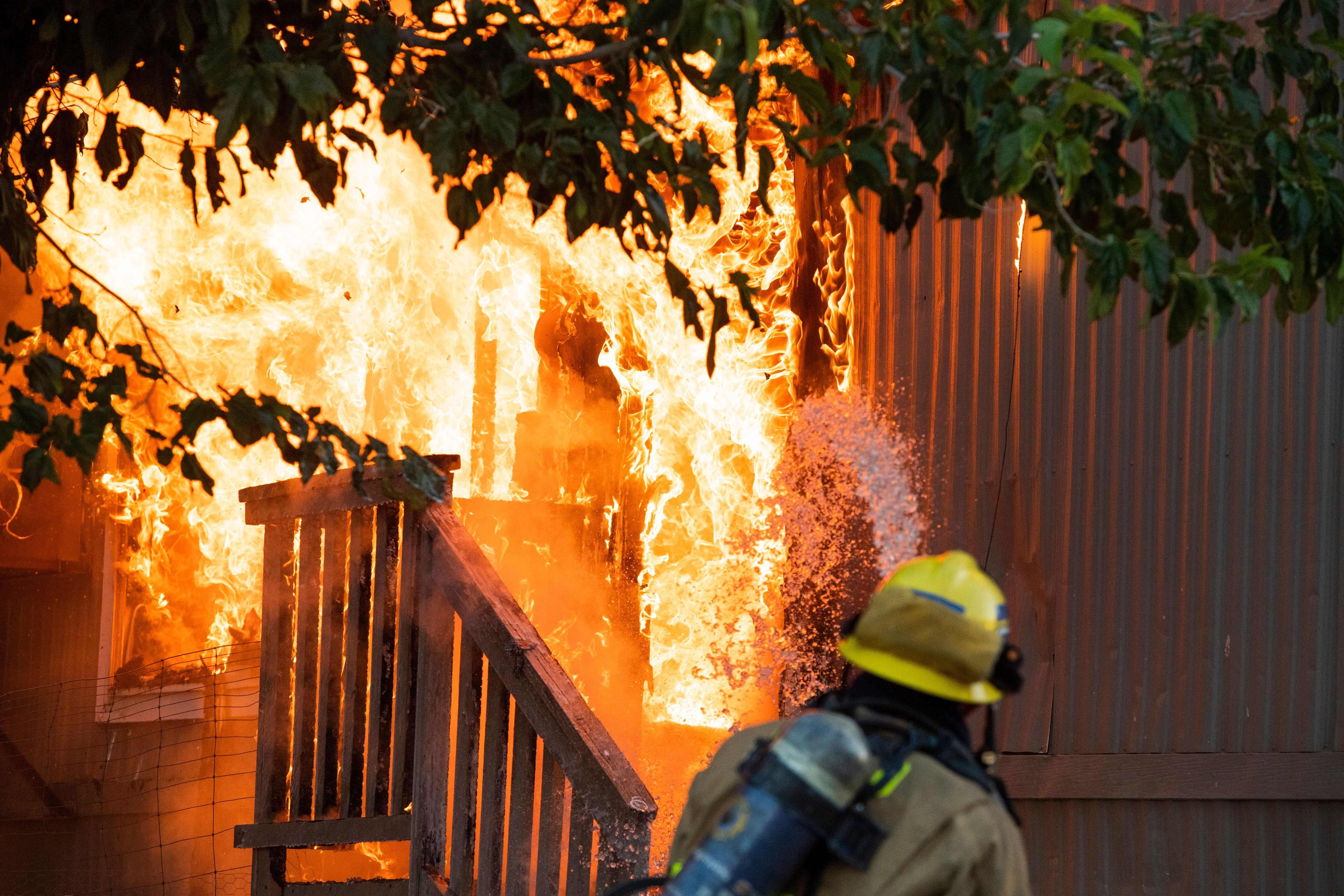 This image shows the back of a fireman's helmet as he stands in front of a burning porch.
