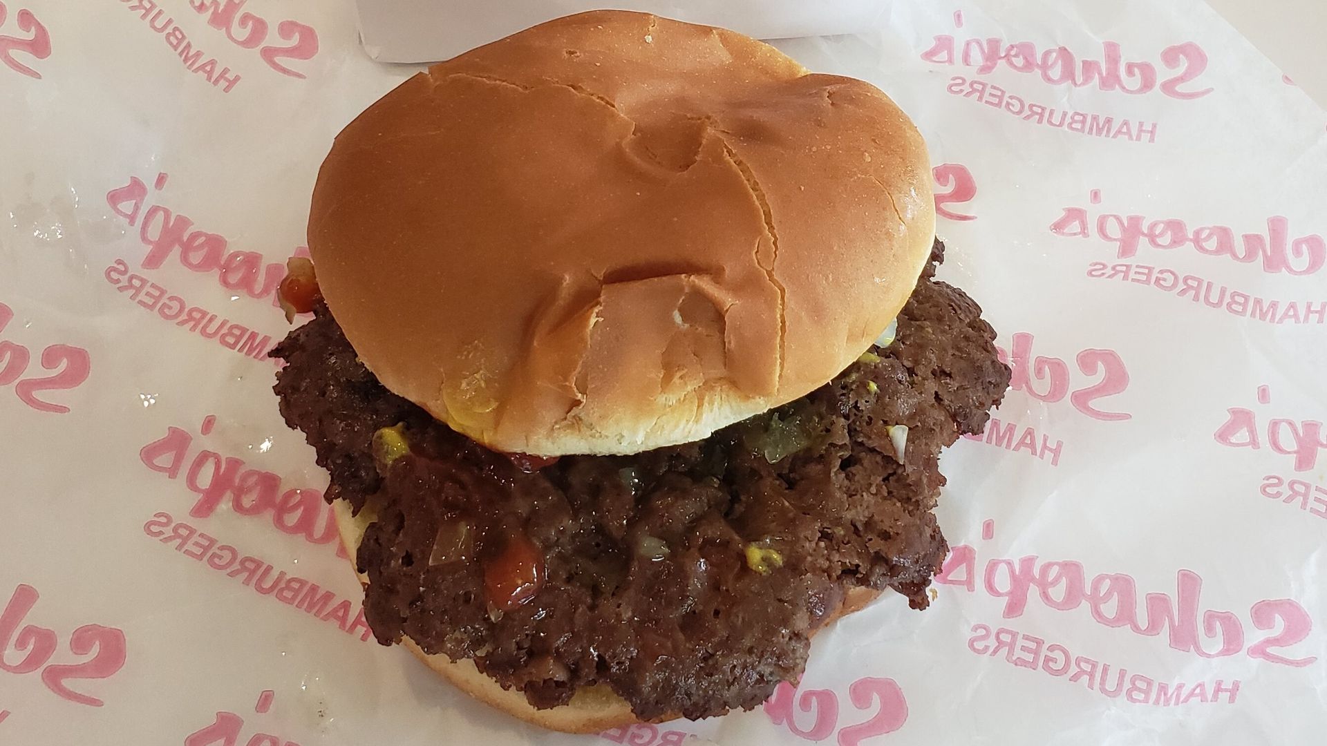 Burger with patty coming out of bun, sitting on wax paper.