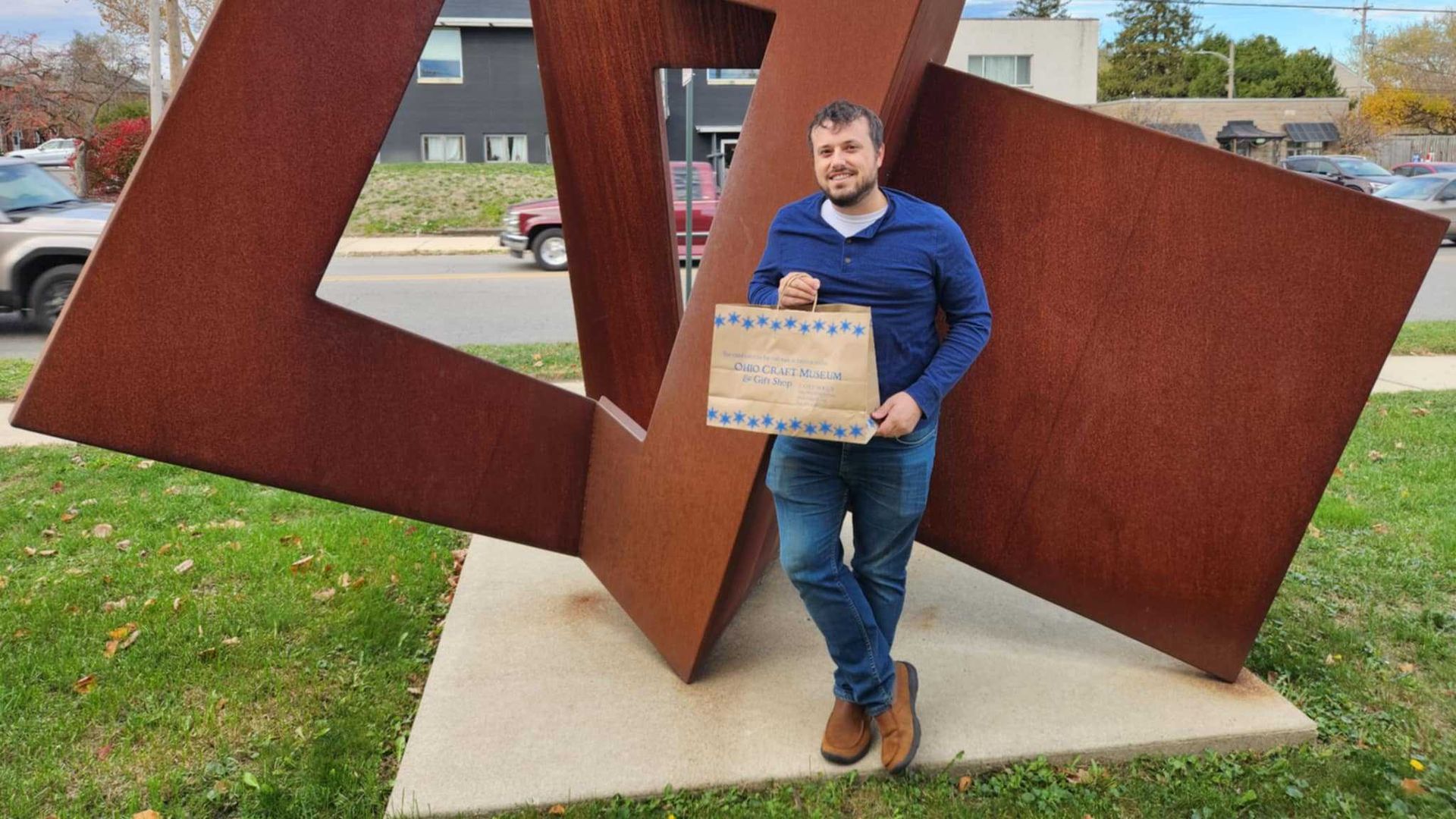 Tyler stands in front of a sculpture while holding a bag of purchased crafts. 
