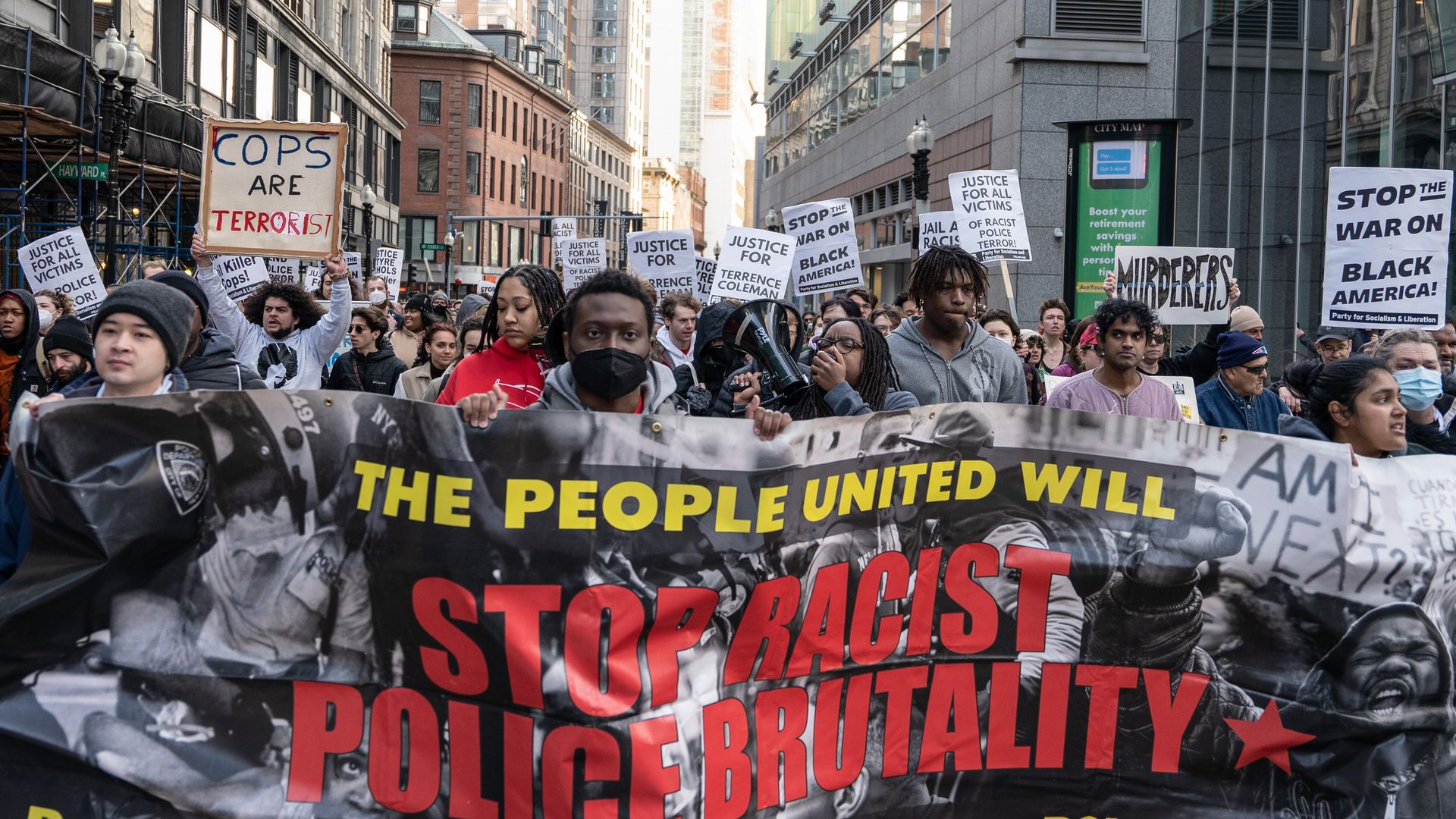 Countless people with signs stand march with a banner in front that says "The people united will stop racist police brutality."