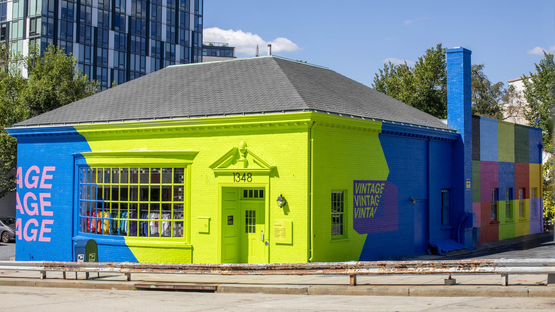 Corner building with bright lime green and blue painted walls featuring the word "VINTAGE" and clothing displayed in large front windows, under a gray shingled roof.