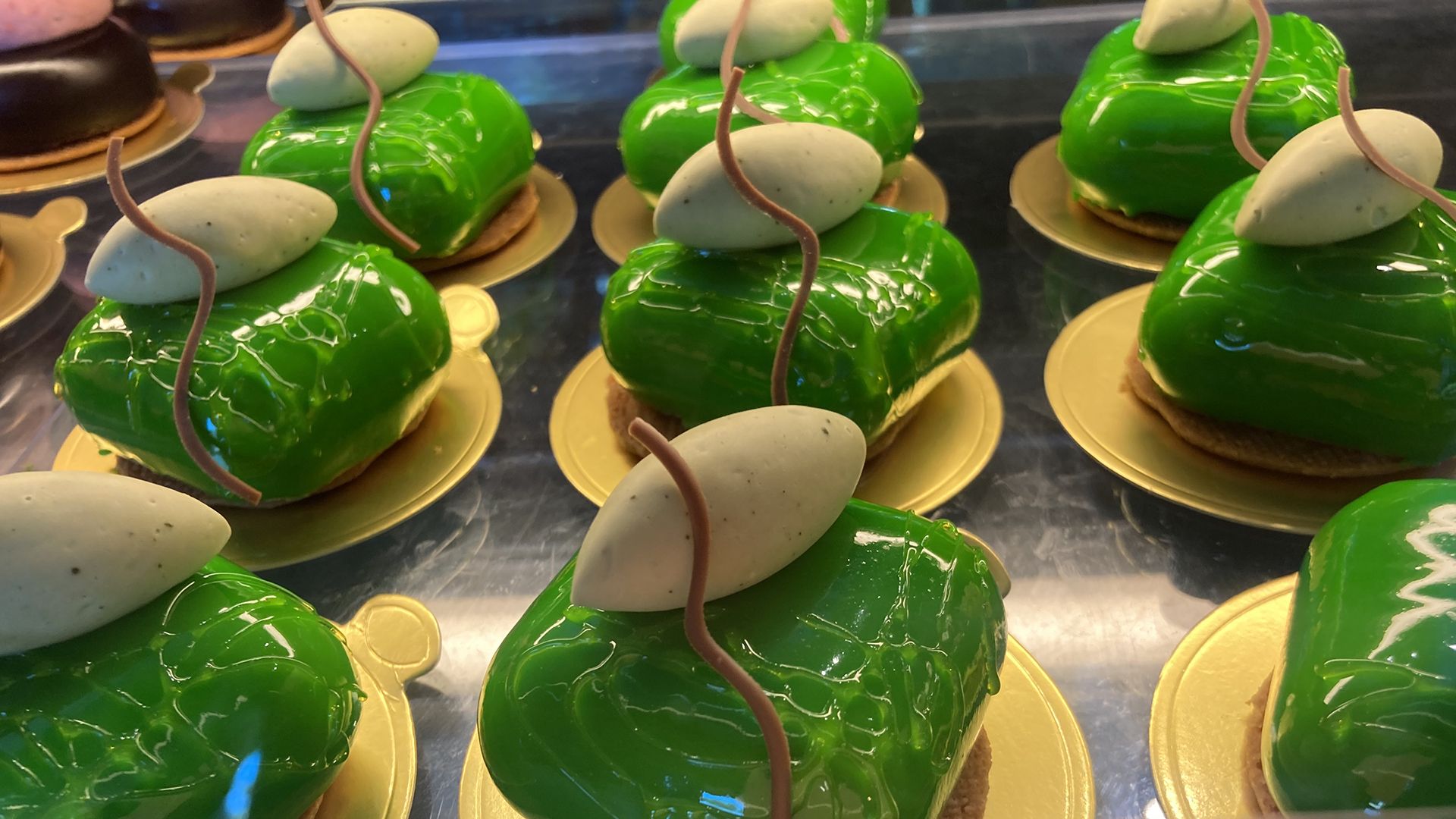 Bright green pastries with a dollop of creamy mousse and a drizzle of chocolate on top sit in a bakery case with a small pink sign that says matcha and yuzu, $9.50