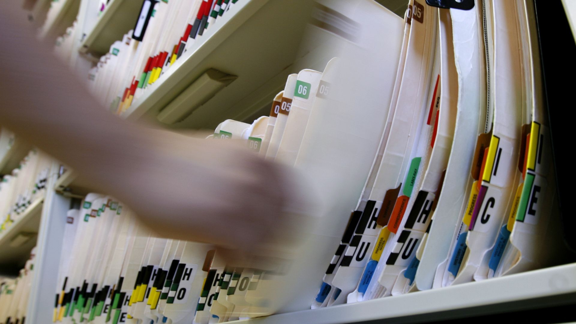 A person picks up a medical chart from a long row in a cabinet.