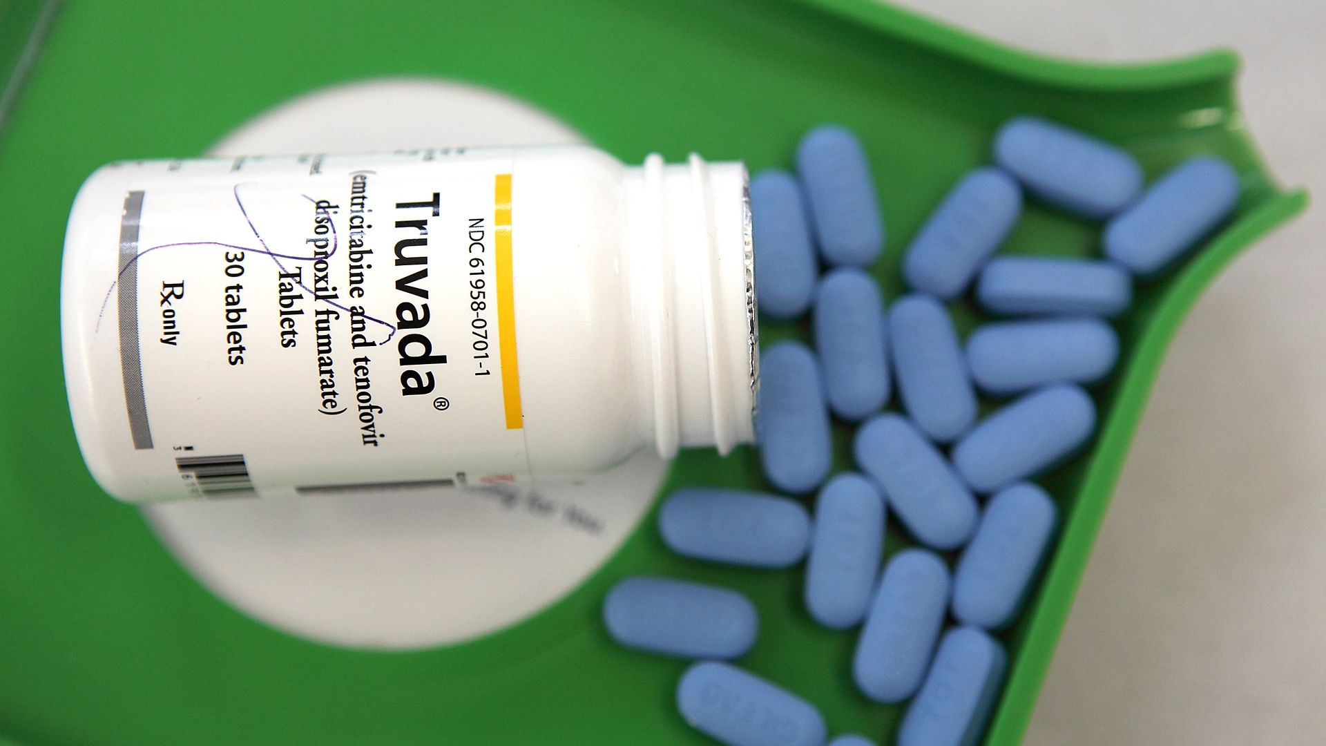 In this image, blue pills spill out of a Truvada pill bottle and onto a green pharmaceutical counting tray.