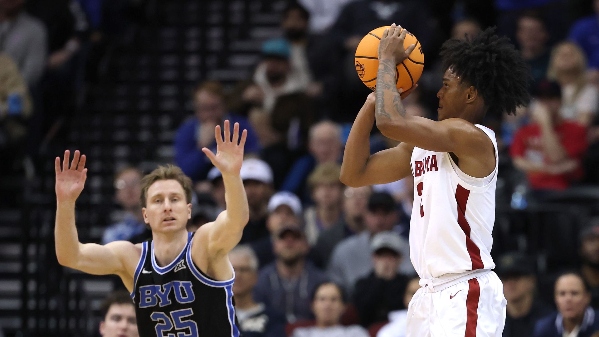 A man in a black jersey contests a jump shot in basketball