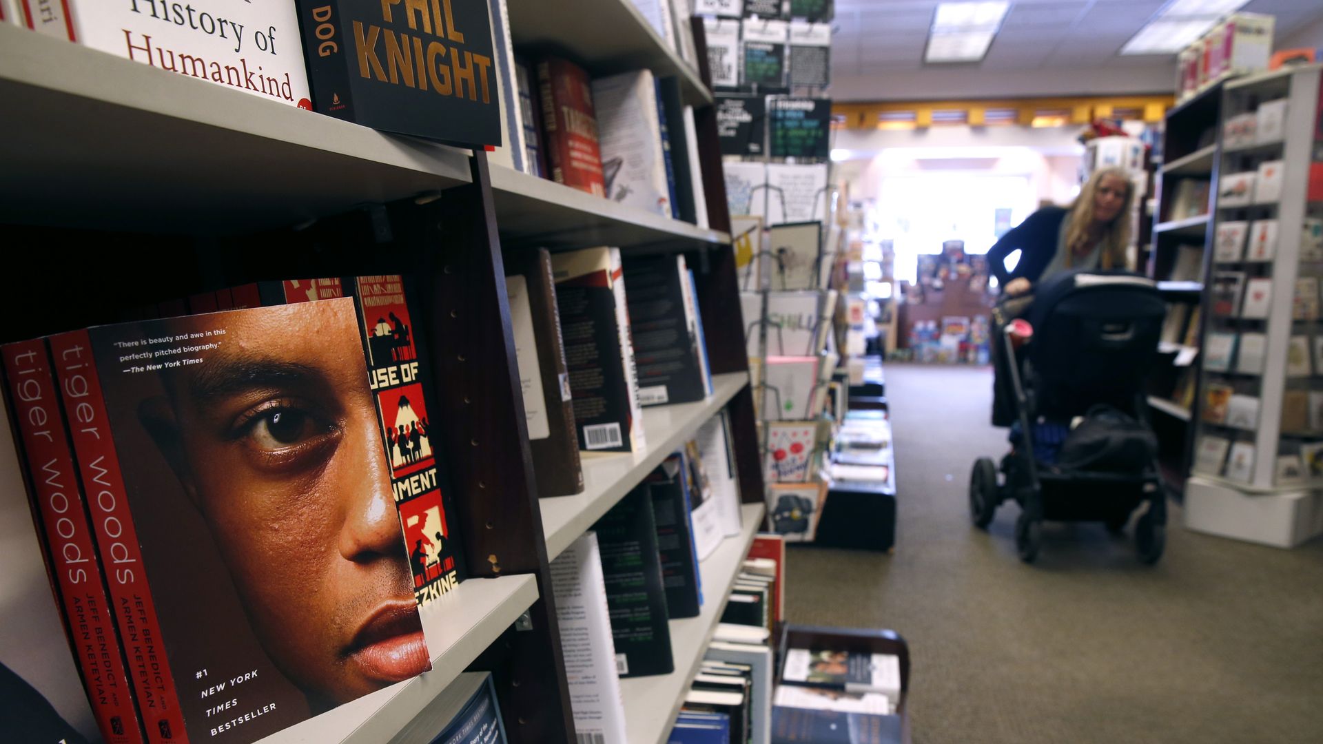 Photo of rows of bookshelves as a person pushes a cart through a booktsore