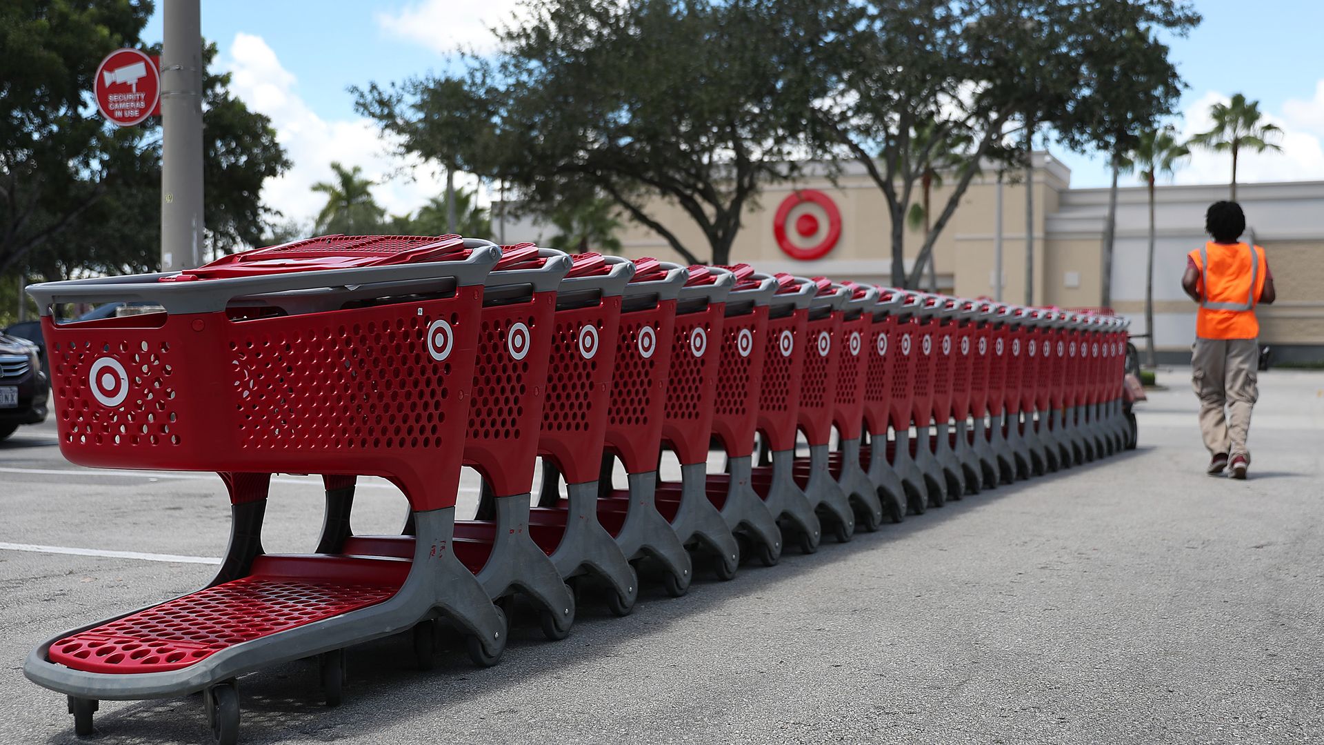 In this image, a Target employee in an orange vest stands next to a line of Target shopping carts.
