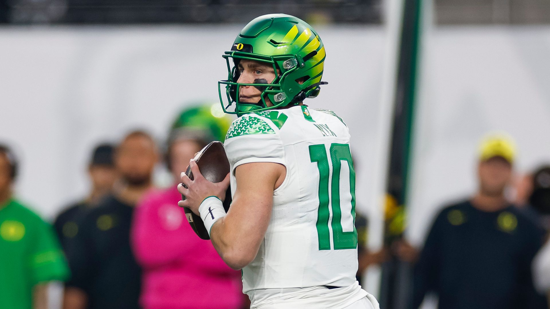 A man in a white jersey and a bright green helmet holds an American football, preparing to throw it.