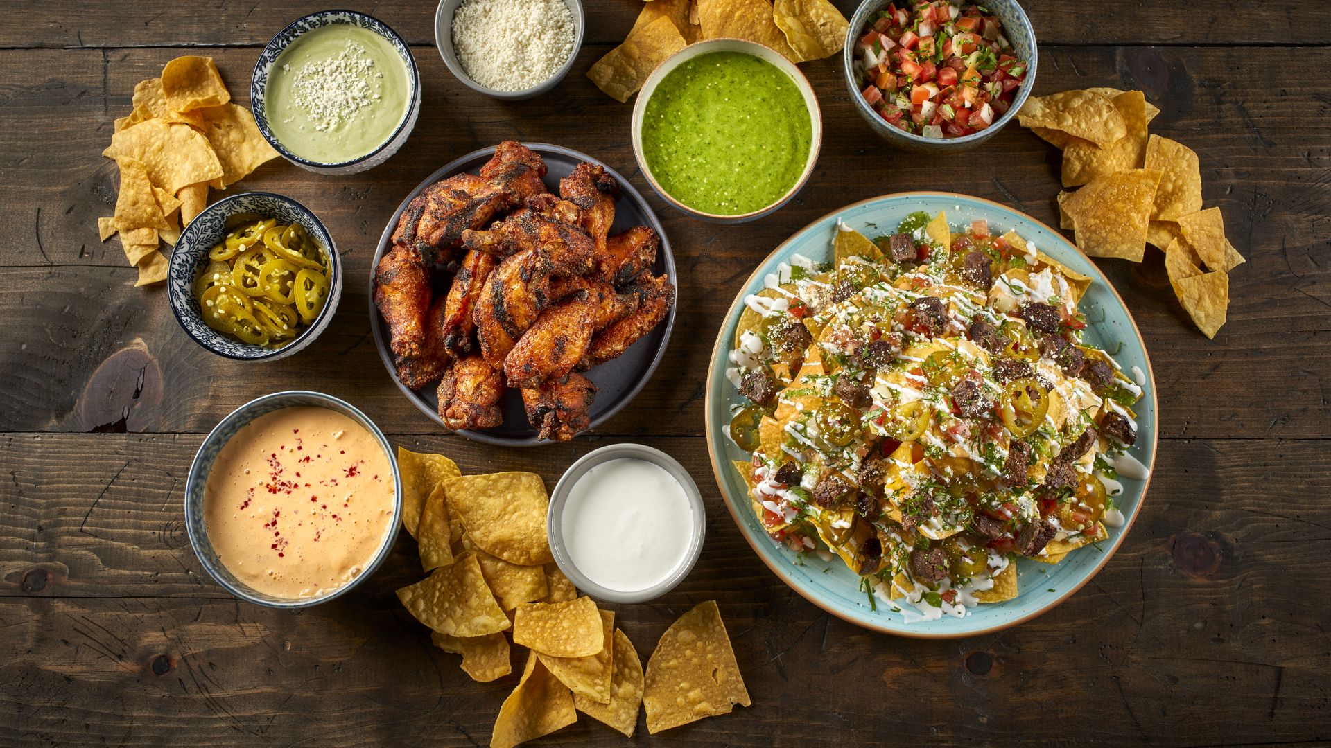 A wooden table with queso, wings and nachos at Taco Bamba