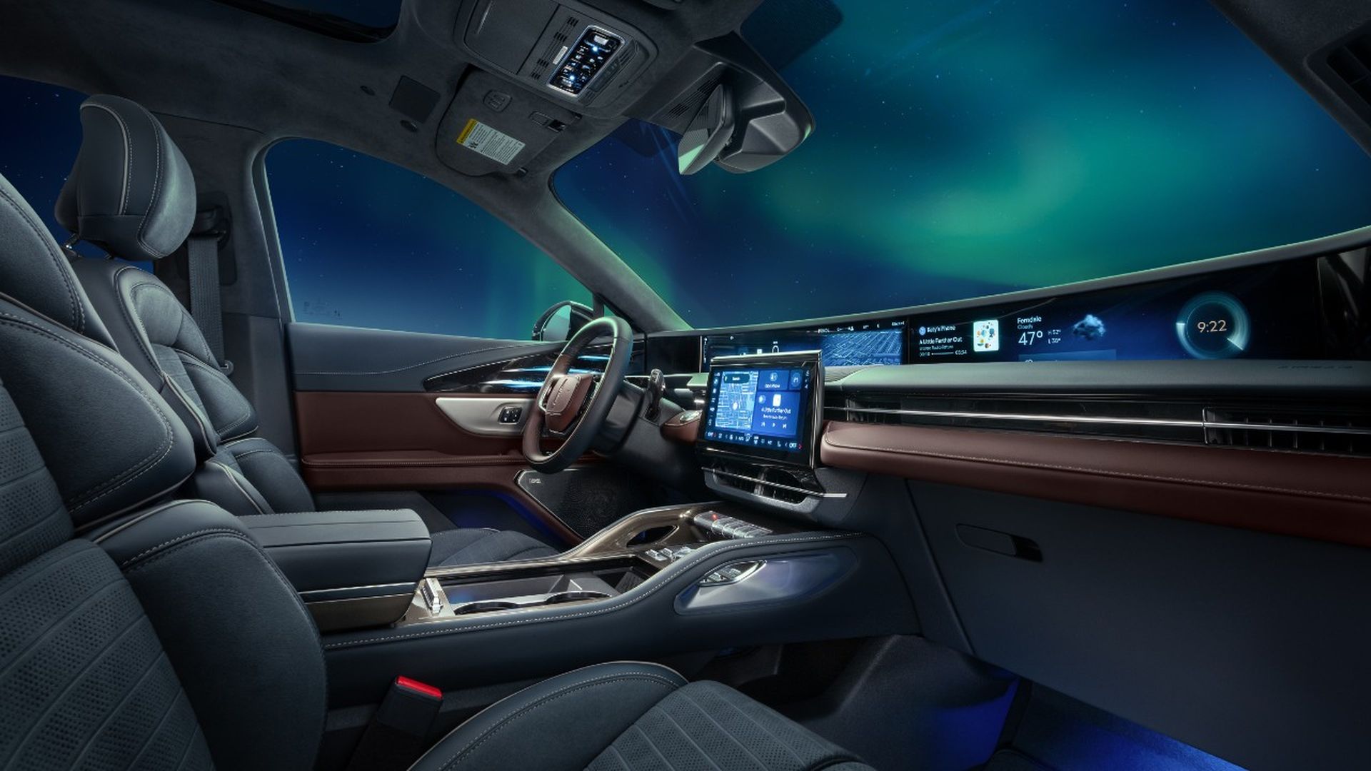 Luxurious interior of Lincoln Nautilus with a wide digital dashboard, center touchscreen, gray leather seats, brown trim, and an aurora-lit sky visible through the windows.