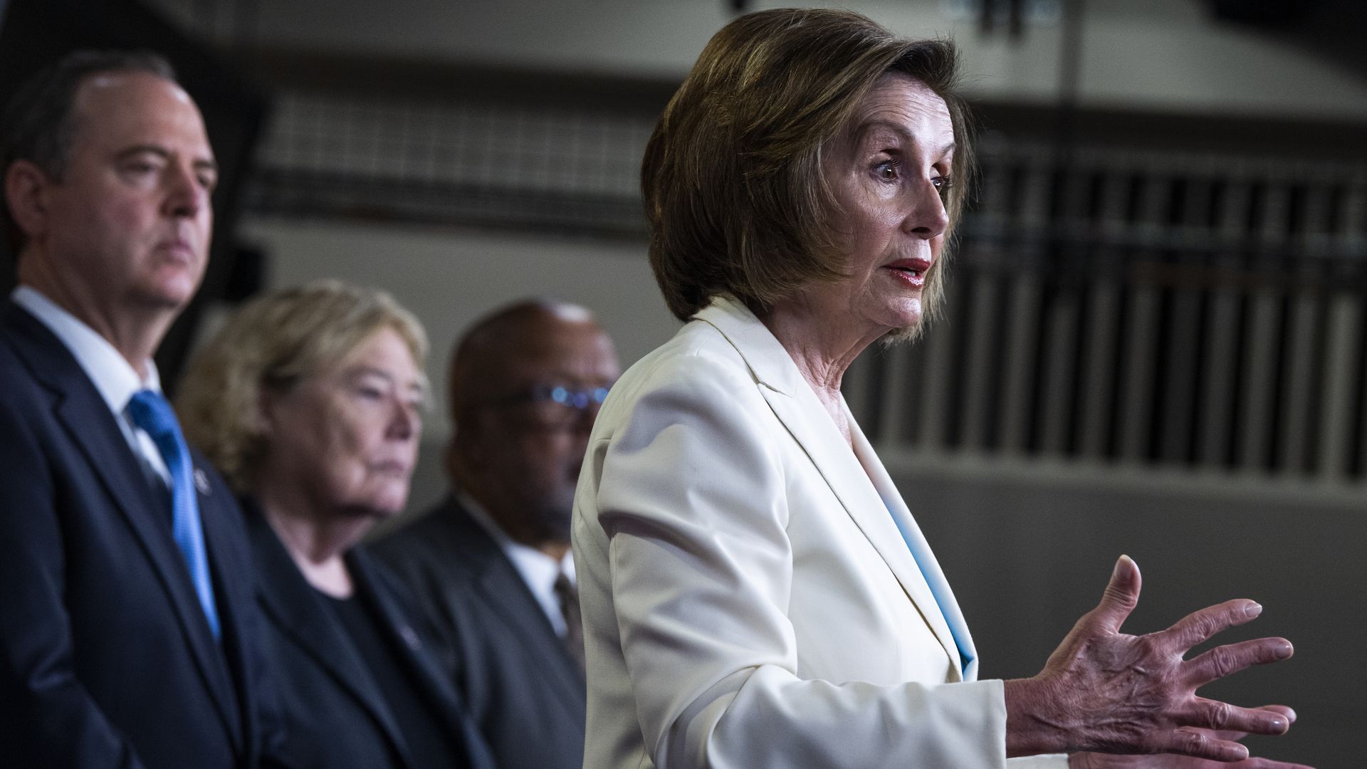 House Speaker Nancy Pelosi, in a white suit, addresses reporters.