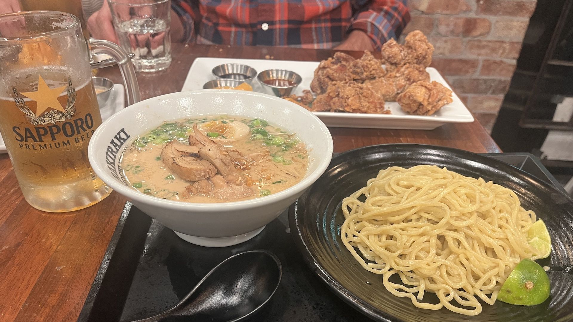 A ramen soup and noodle dish, a sapporo draft beer in a mug and a plate of fried chicken on the table.