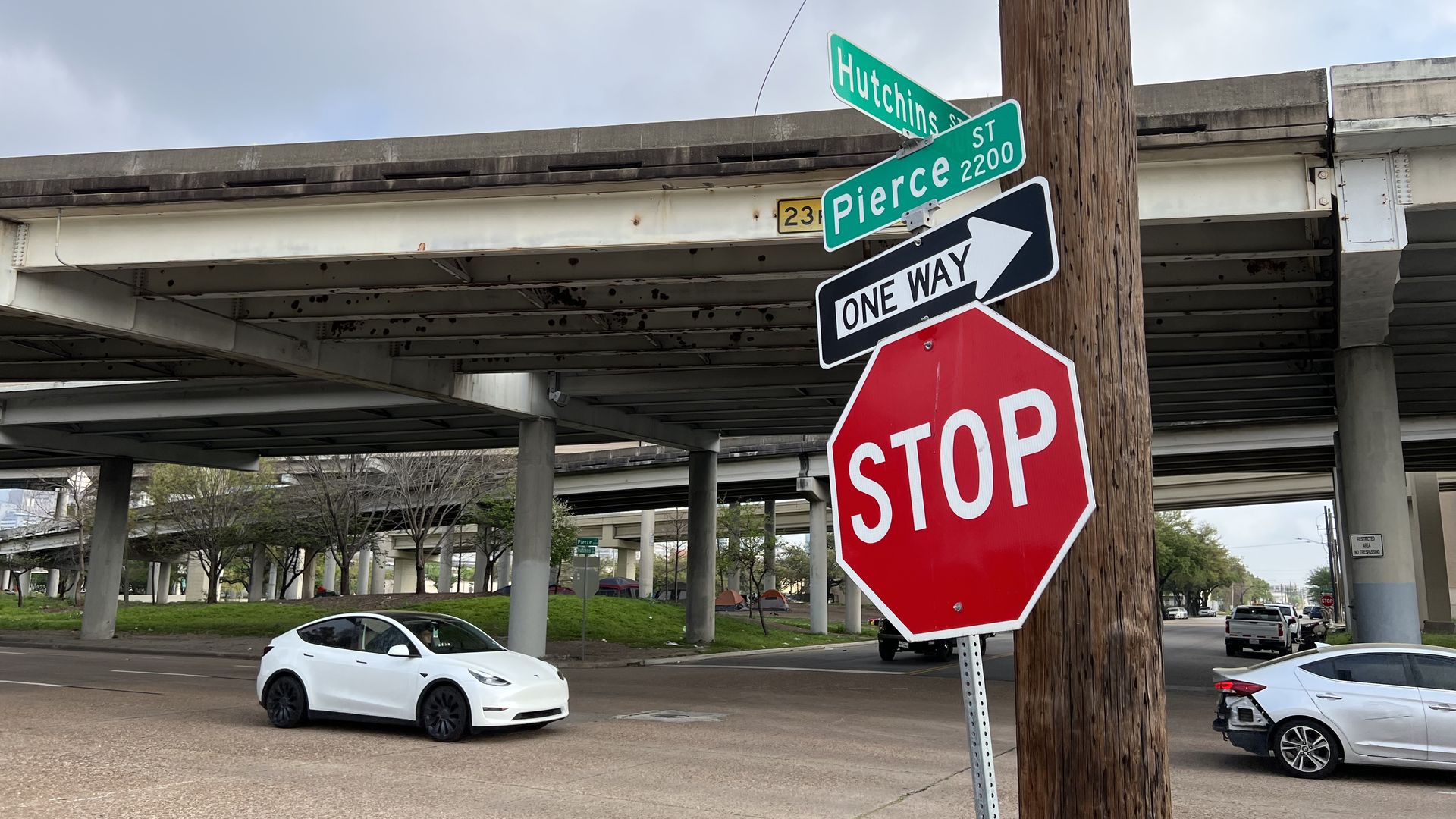 A stop sign at the intersection of Hutchins and Pierce streets in Houston, with a homeless encampment in the background