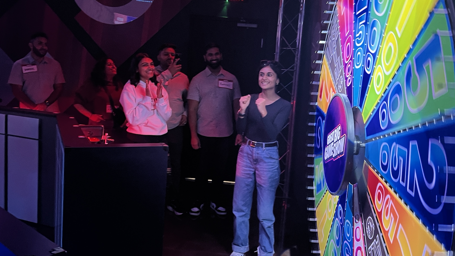 Six people standing next to a spin-the-wheel board with points values
