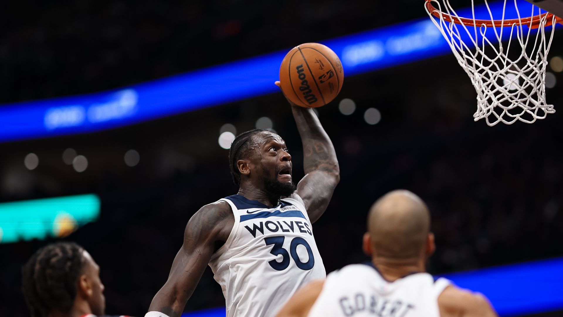 Julius Randle holds a basketball up and prepares to dunk it as a Washington player and Rudy Gobert look on 