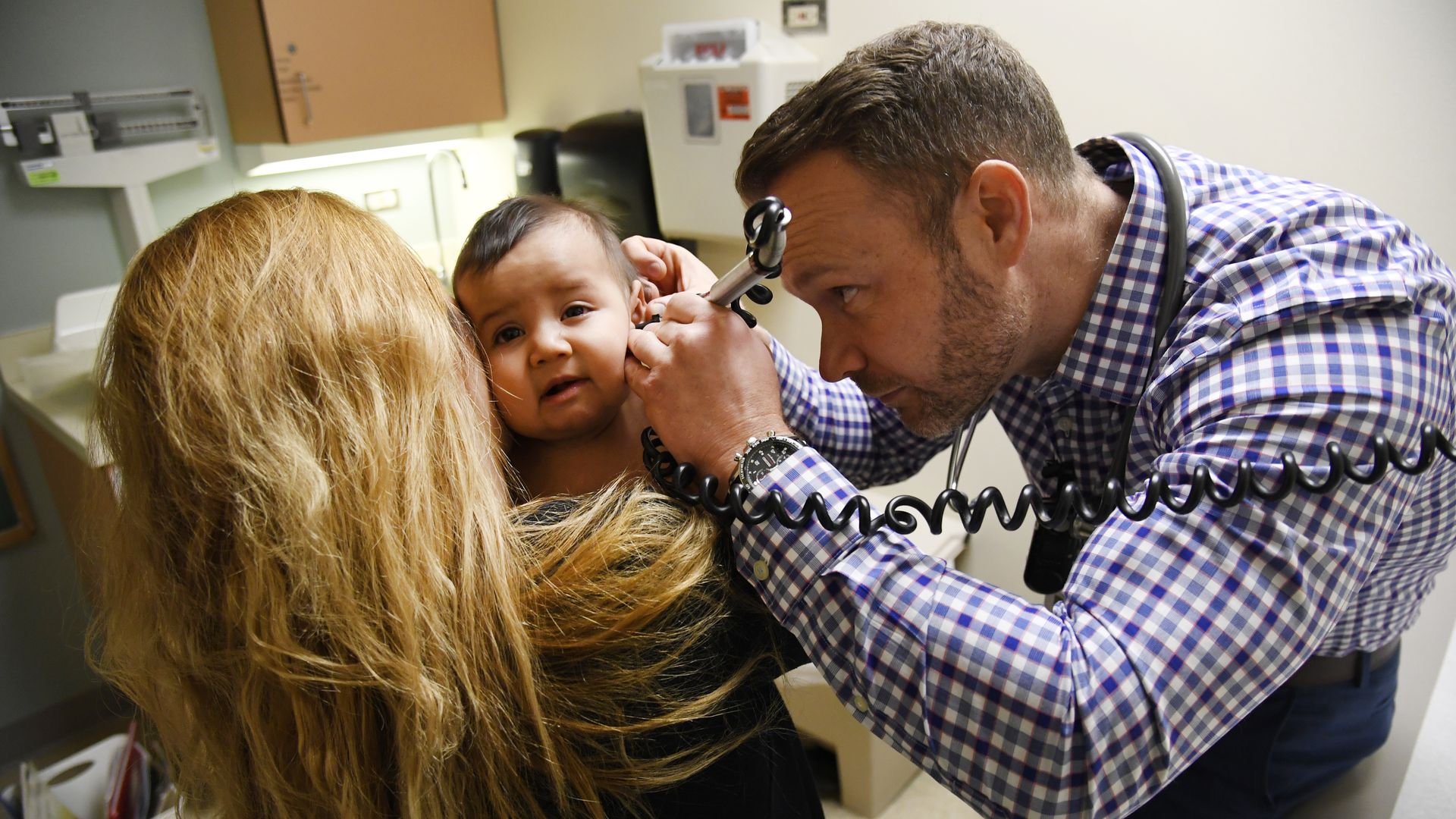 A doctor looks inside the ear of an infant.