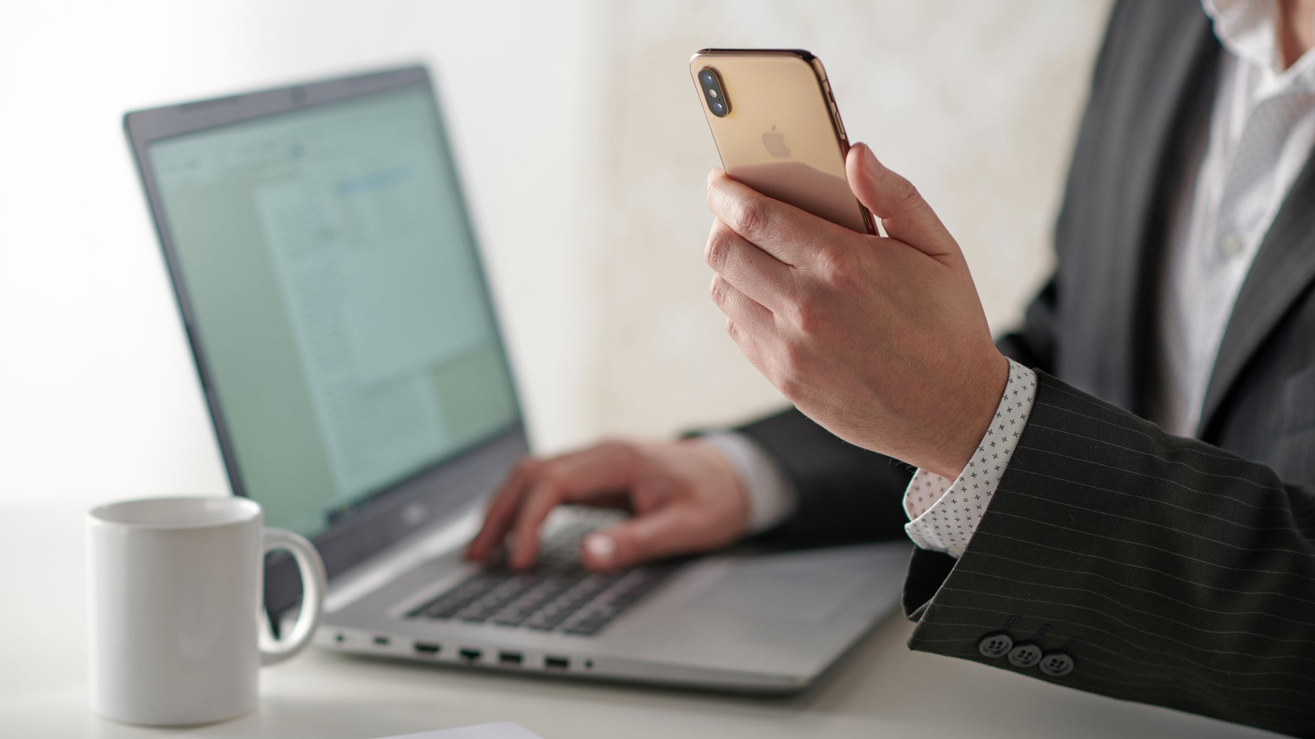Business man looks at his smartphone while working on his laptop.