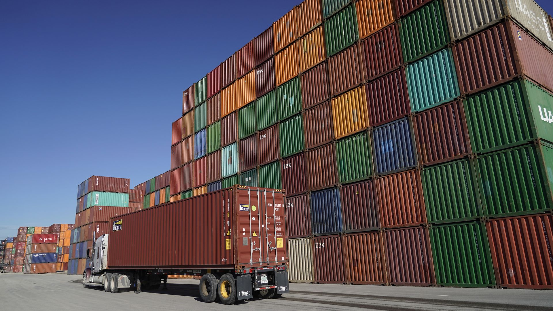 A trailer truck next to a stack of containers.