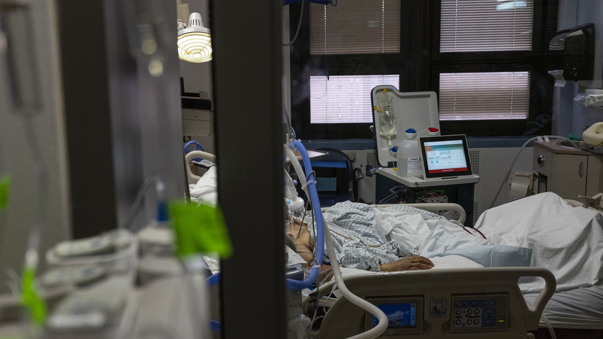 A patient lays in a hospital bed surrounded by a ventilator and other medical supplies.