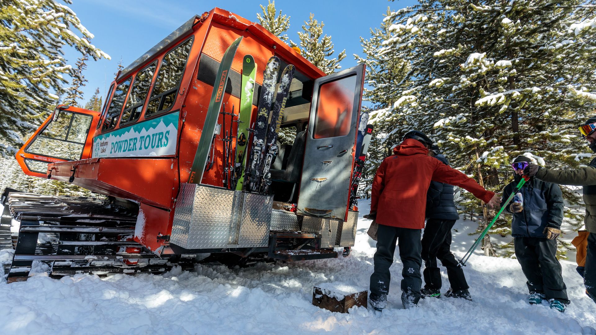 A group of people stand next to a large vehicle on tank treads in a snowy forest.
