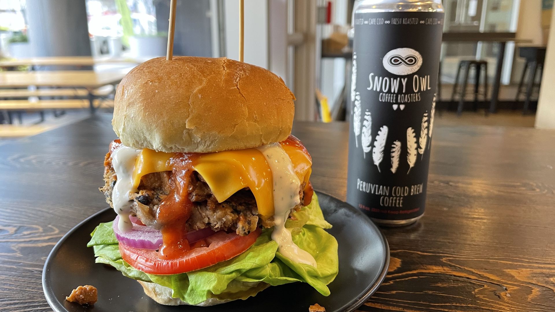 A massive veggie burger with lettuce, tomato, onion, yellow cheese, guacamole and ranch dressing held together by two skewers.