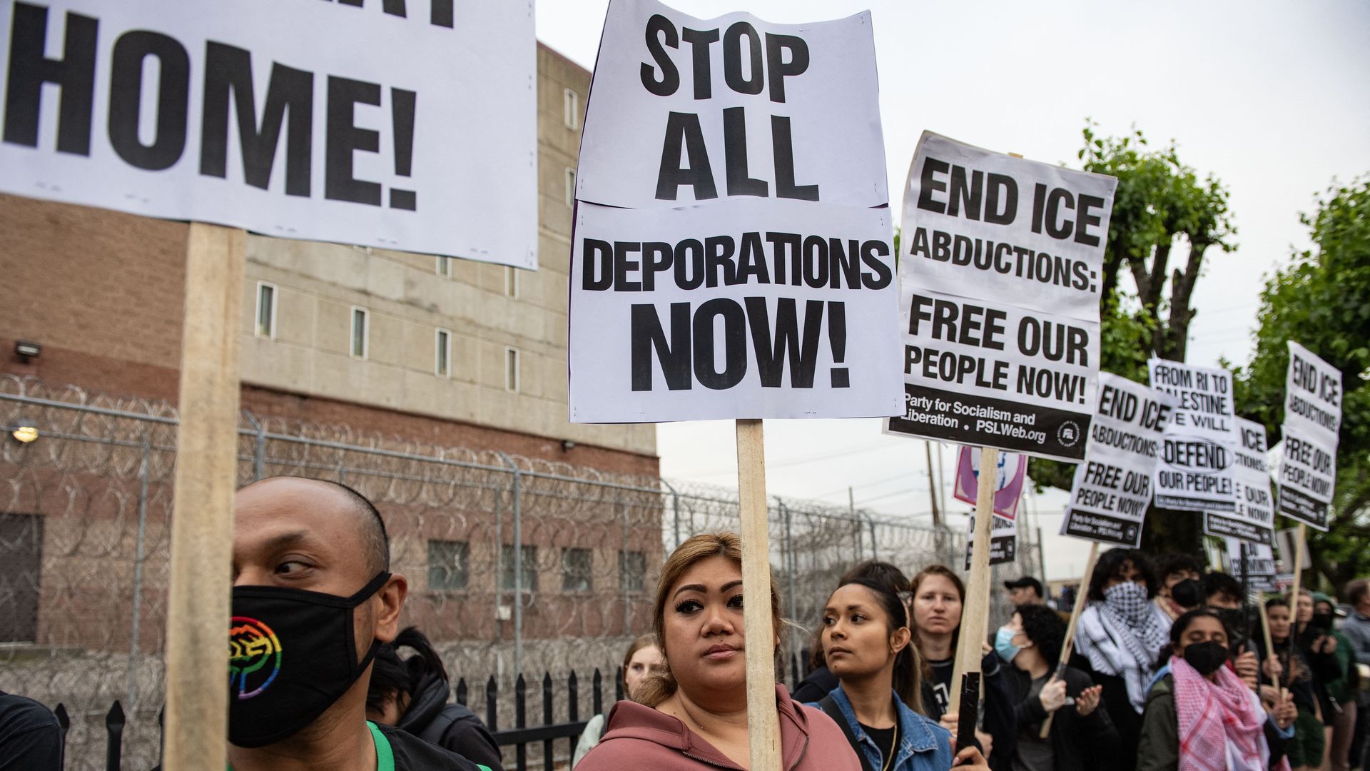 Protesters hold signs that say things like "STOP ALL DEPORTATIONS NOW!" and "END ICE ABDUCTIONS."