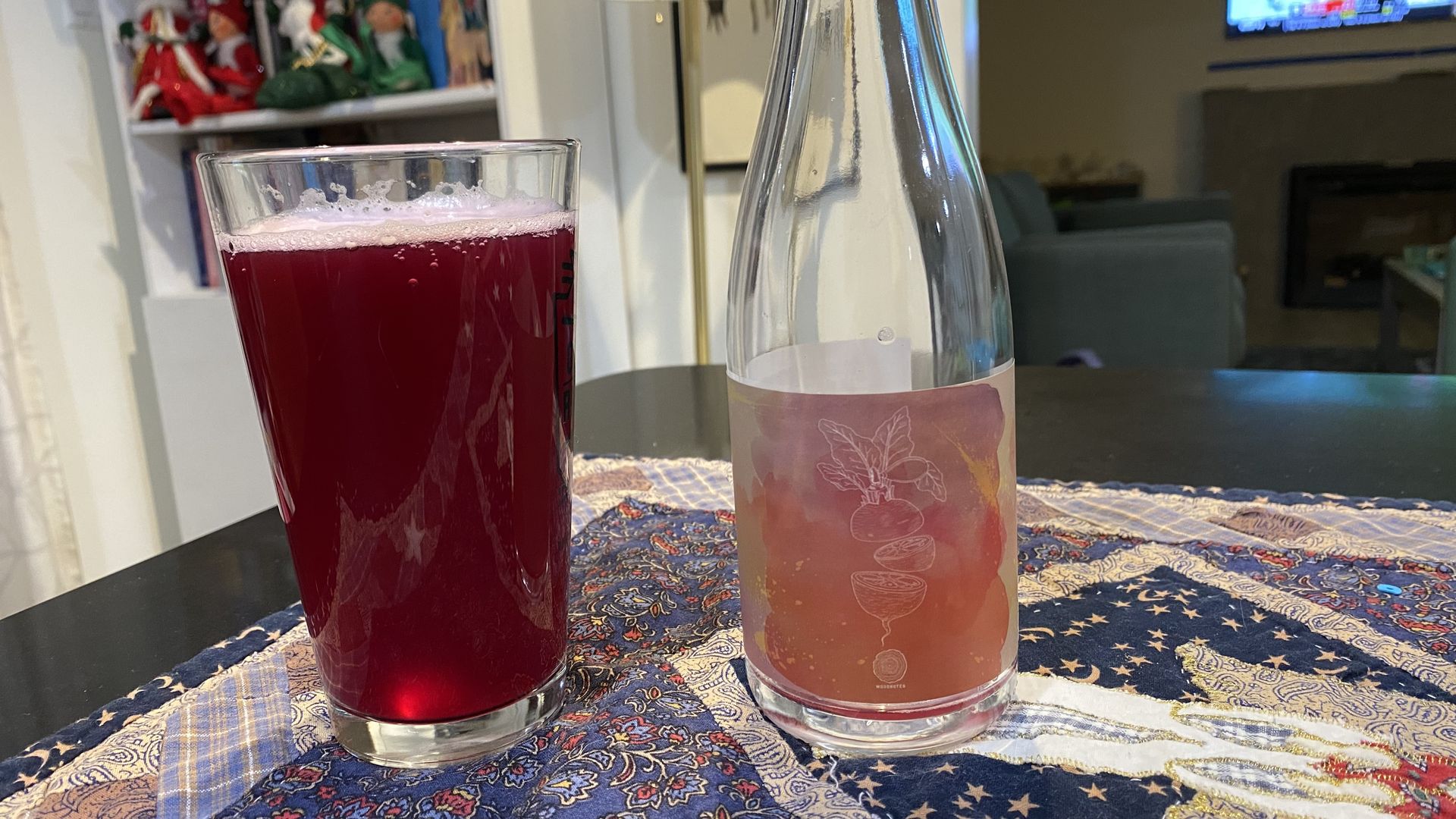 A pint glass of bright magenta liquid and a clear empty beer bottle.
