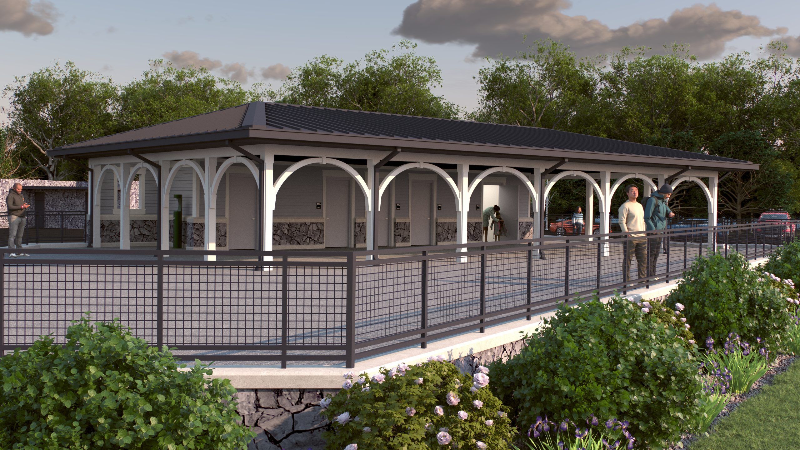 Outdoor pavilion with white arches and stone base surrounded by greenery and flowers, people standing and interacting, under a cloudy sky at dusk.