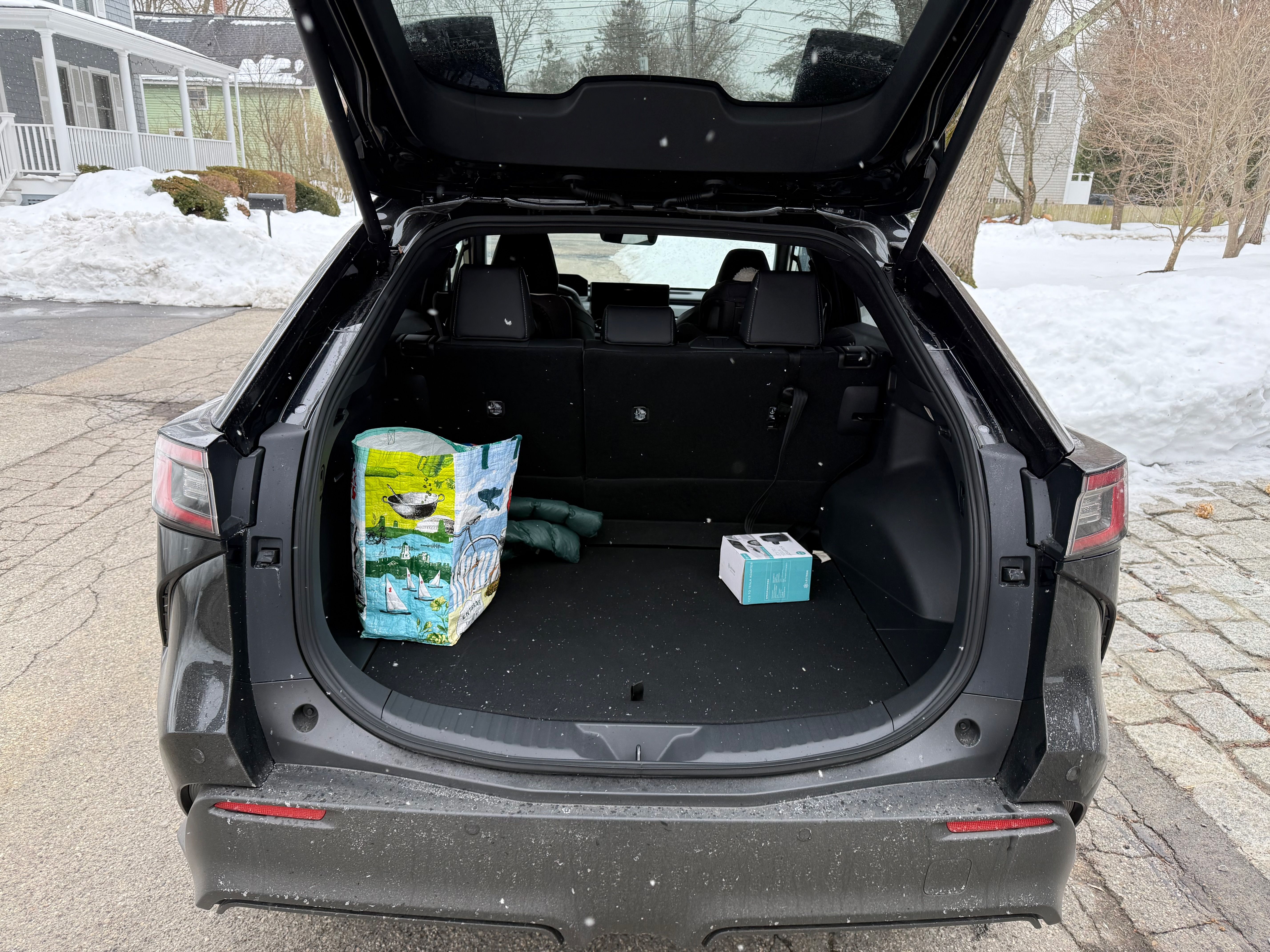 A photo of the Subaru Solterra's rear cargo area, with the hatch lifted, where a blue and green Trader Joe's bag and blue-and-white box sit on black cloth.