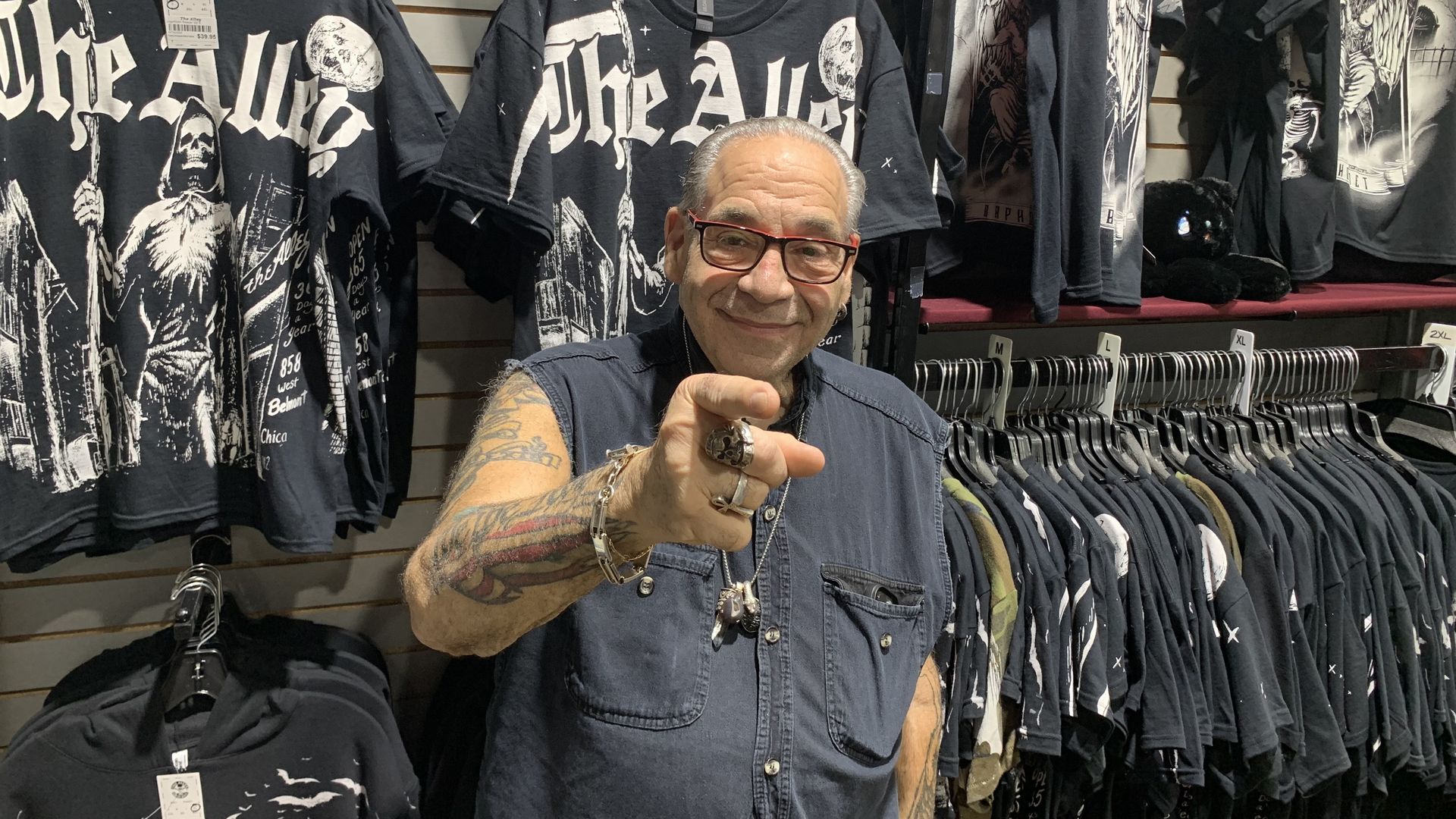 Photo of a man pointing at the camera in front of leather jackets on a wall 
