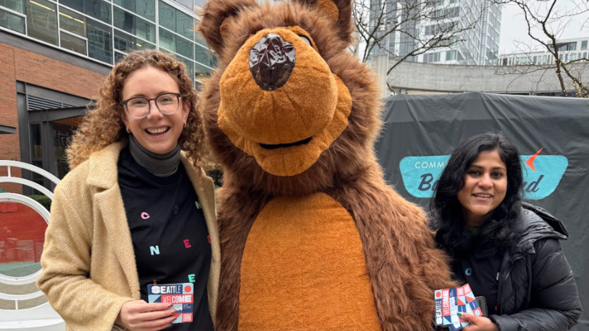 A person in a bear suit flanked by two women in a Seattle neighborhood.