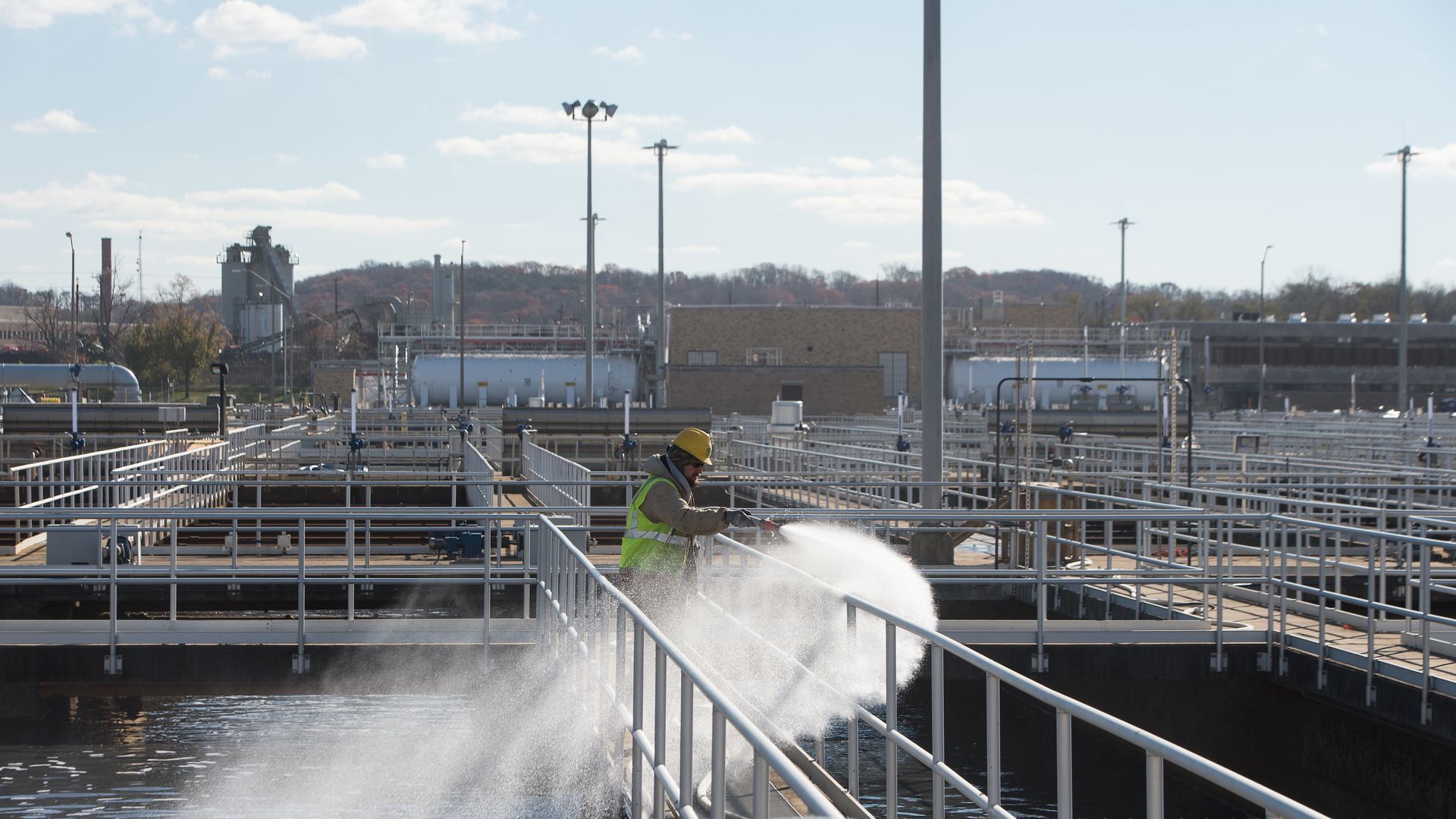 A man sprays water into a pool while standing over a bridge. The pool is filled with wastewater.