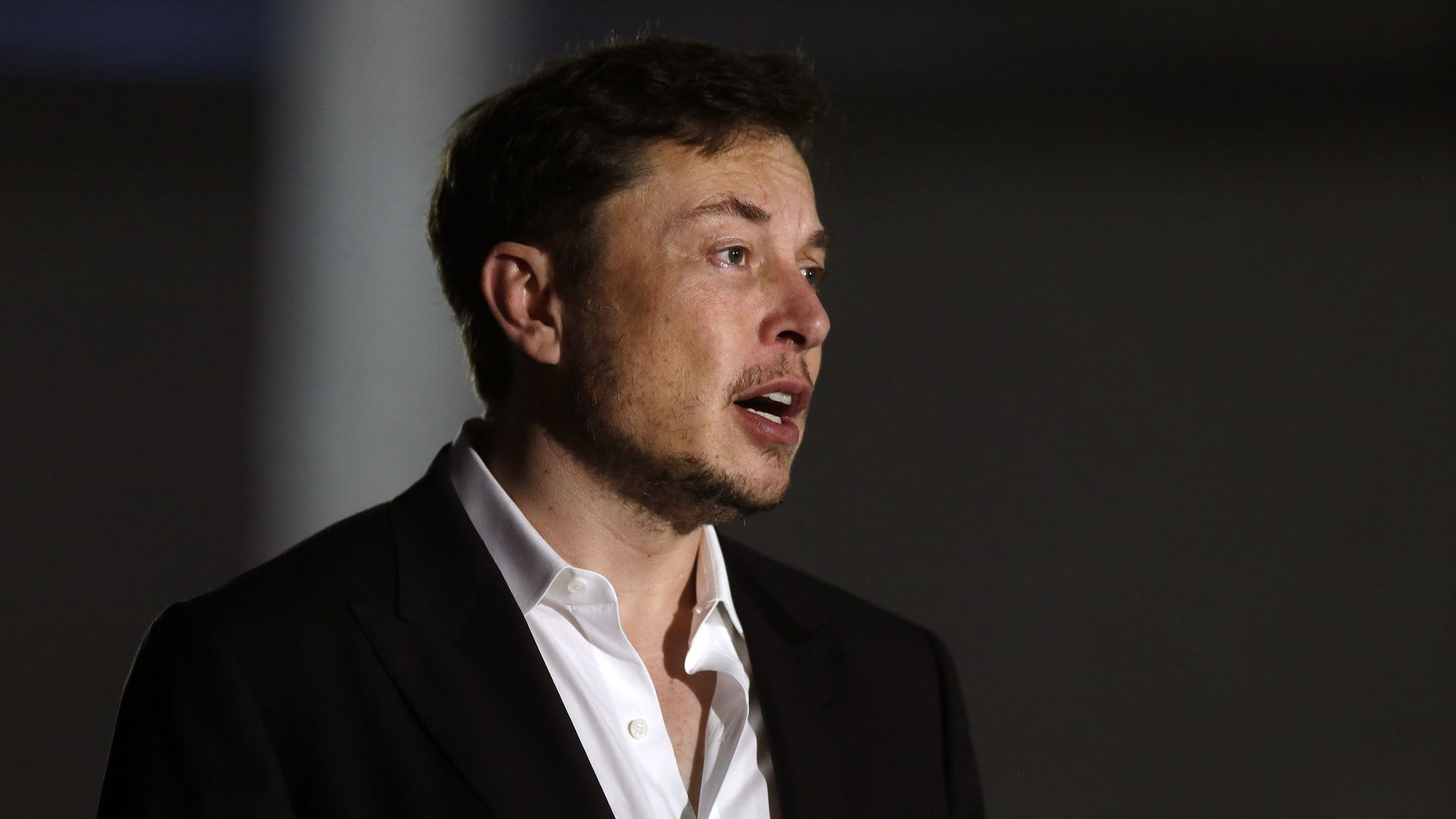 Side profile of Elon Musk talking to a group