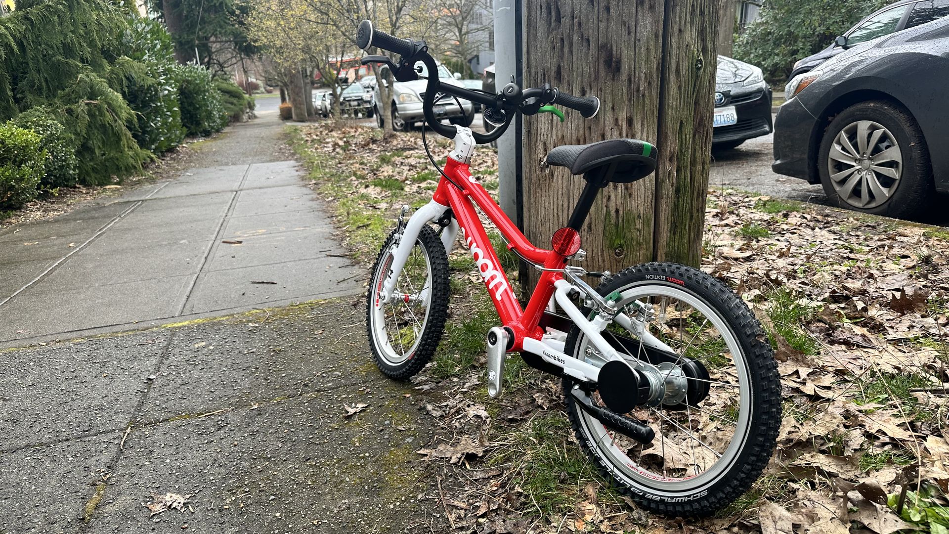 A red bike against a telephone pole situated at the top of a hill next to a sidewalk. 