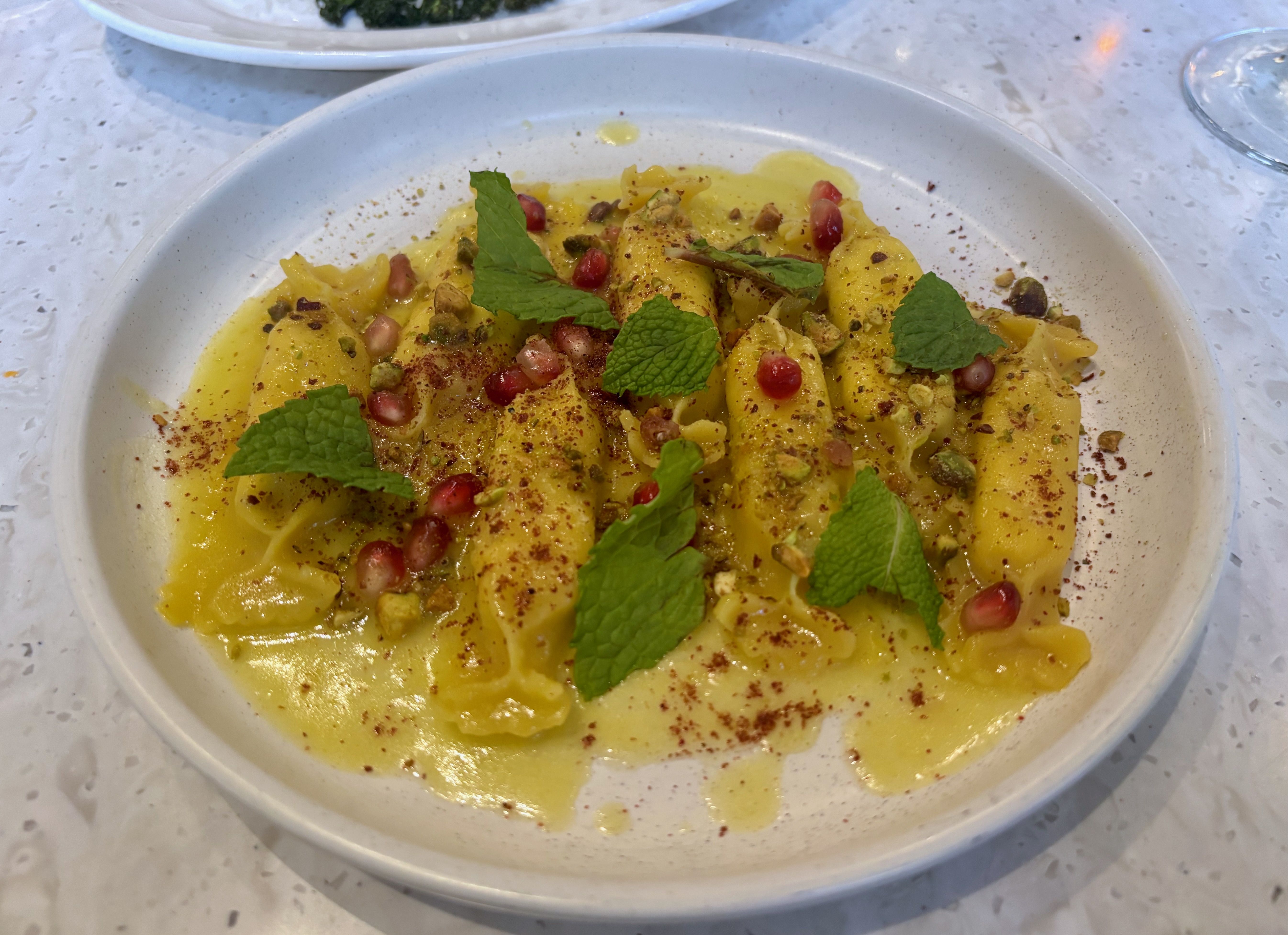 The limone pasta, shaped like yellow candy wrappers, topped with mint leaves, pomegranate seeds and a yellow sauce