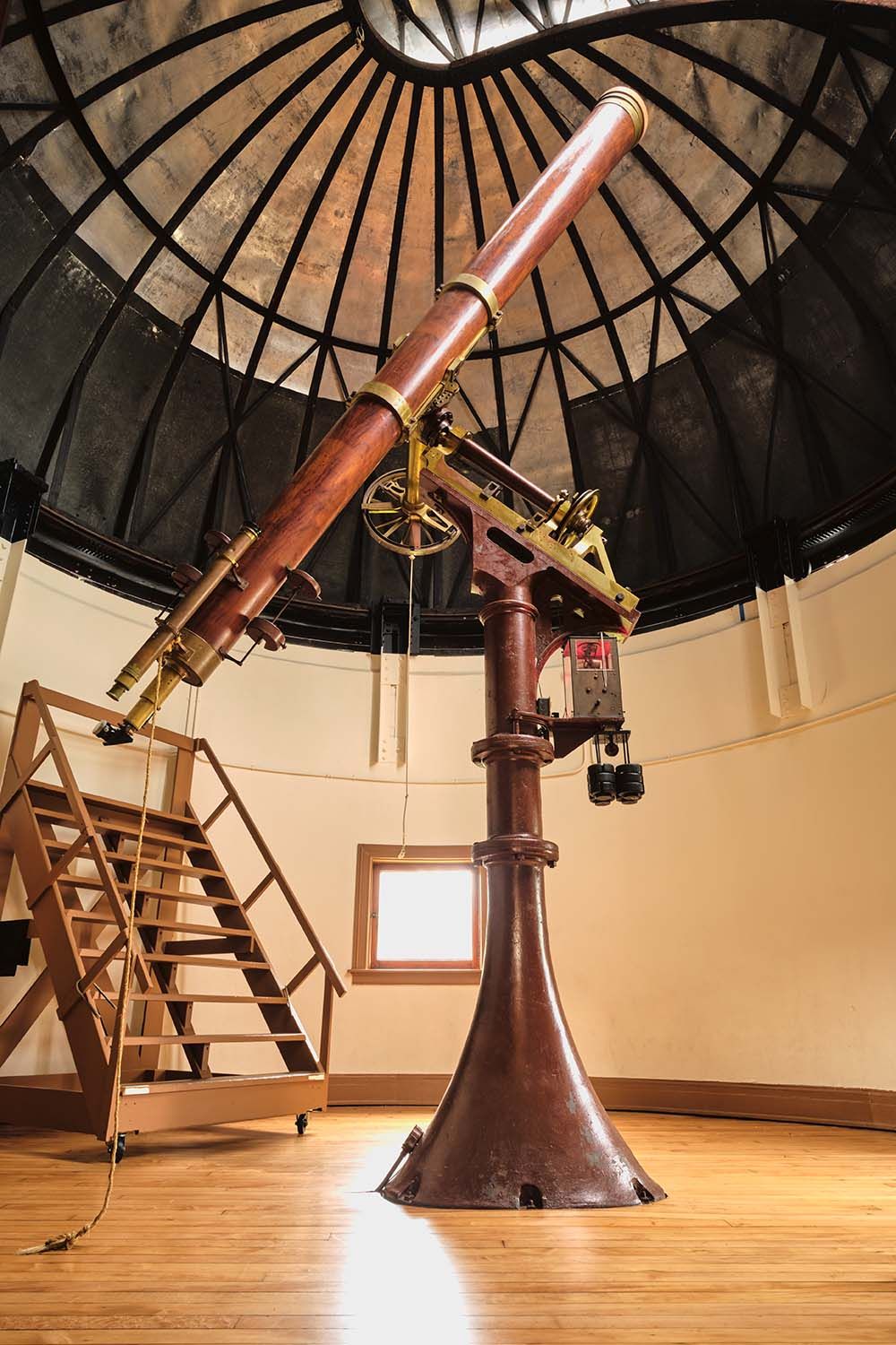 A long telescope sits atop a pedestal inside a domed observatory.
