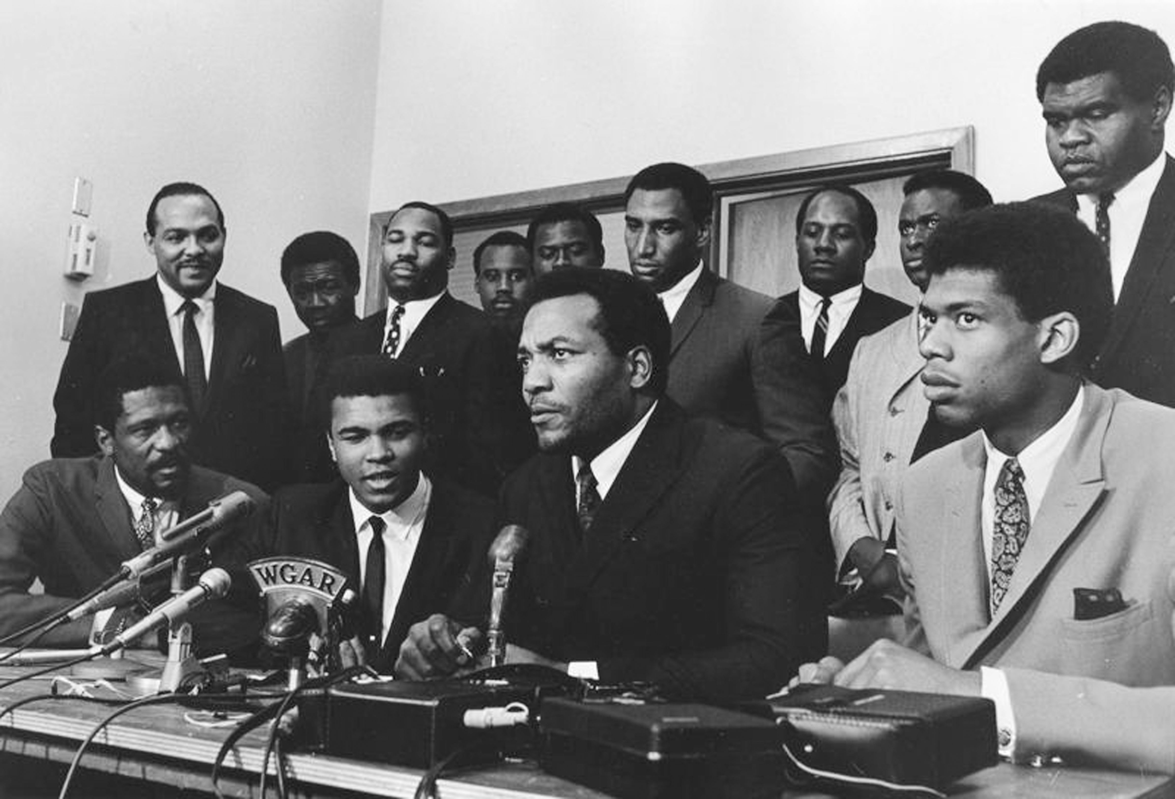 Black athletes in suits before microphone in 1967