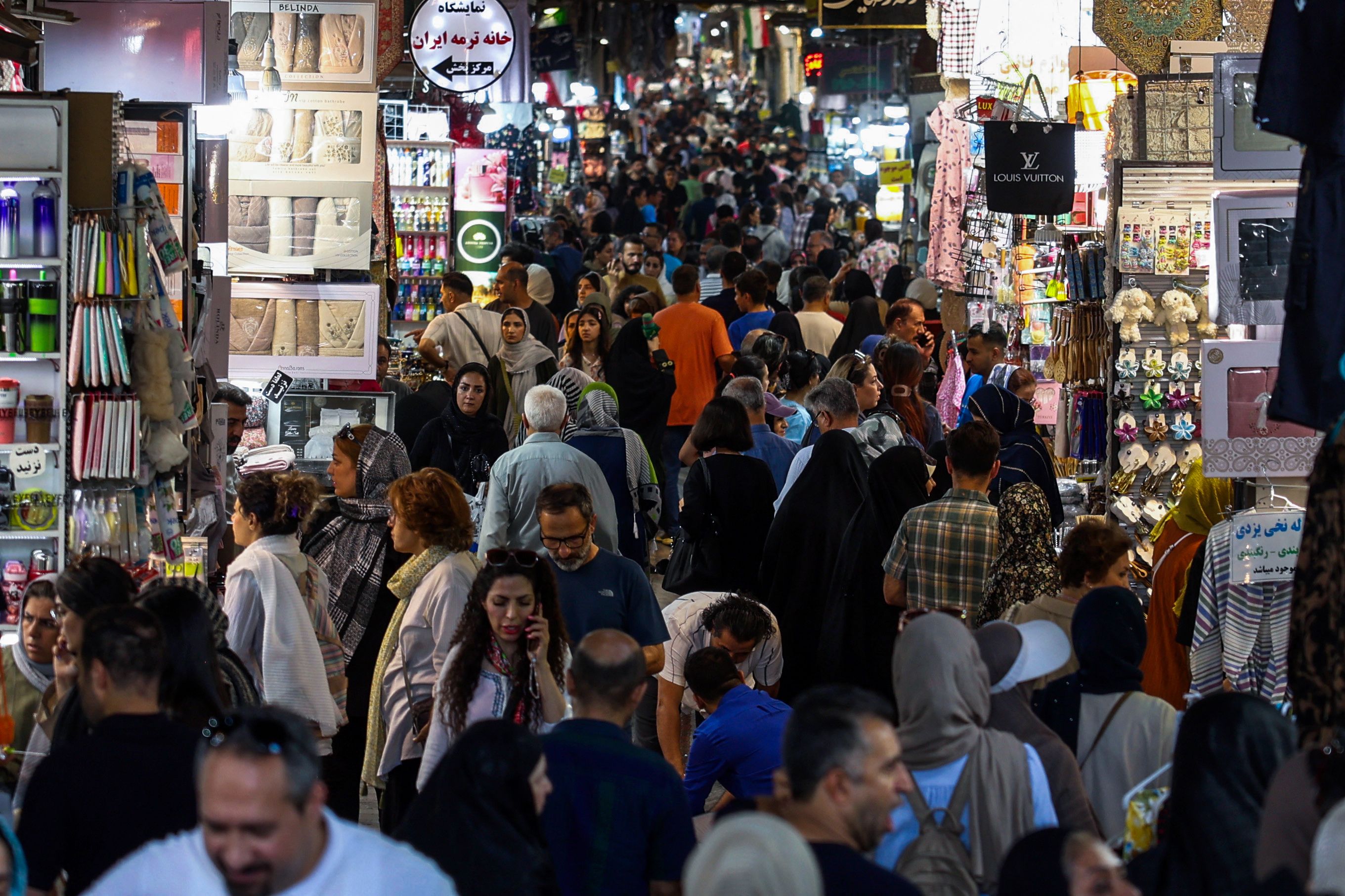 People walk through Tehran’s Grand Bazaar past shops displaying goods.