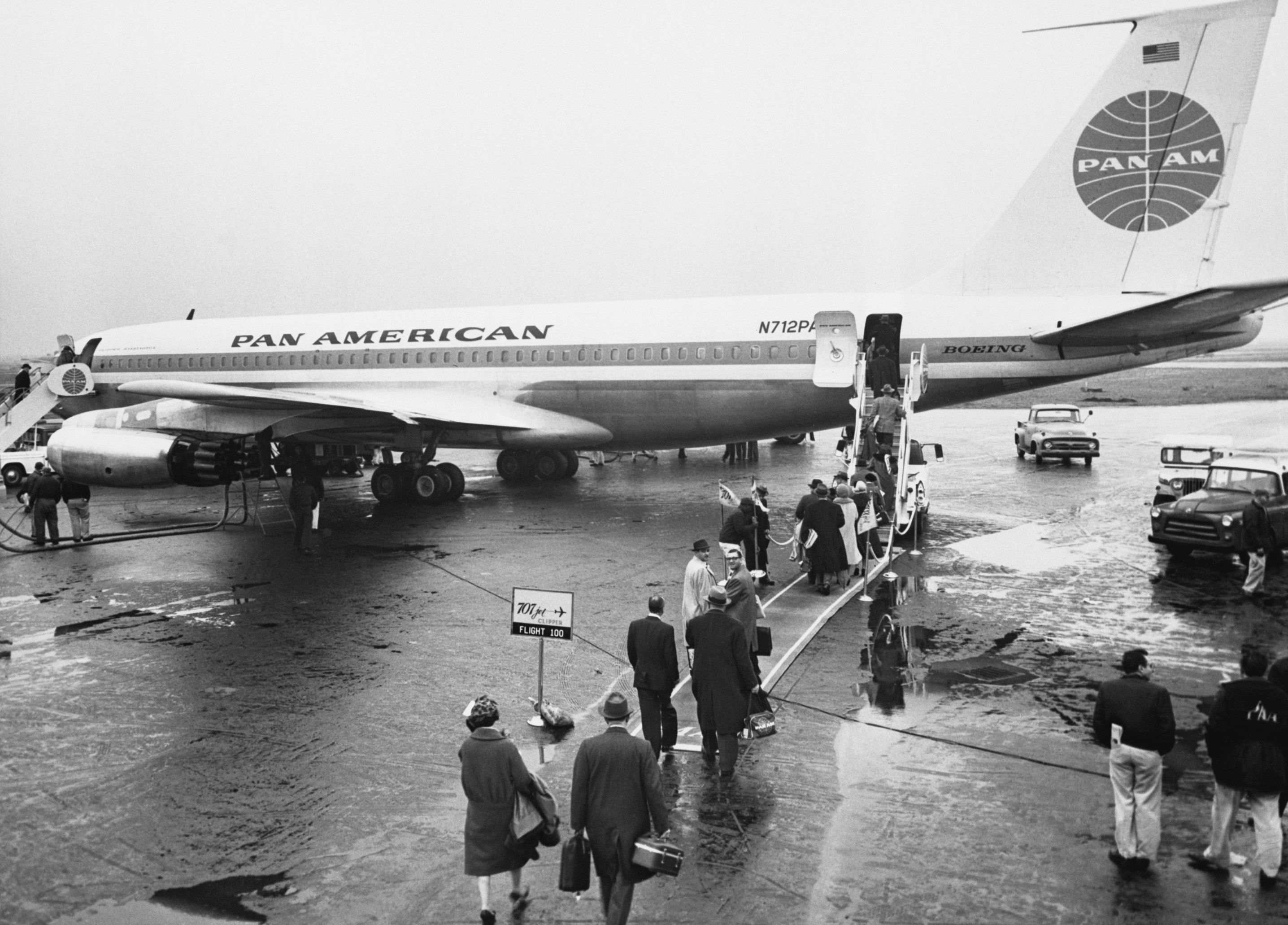 Black and white photo of passengers lined up on a tarmac to board a plane that says "Pan American" on the side.