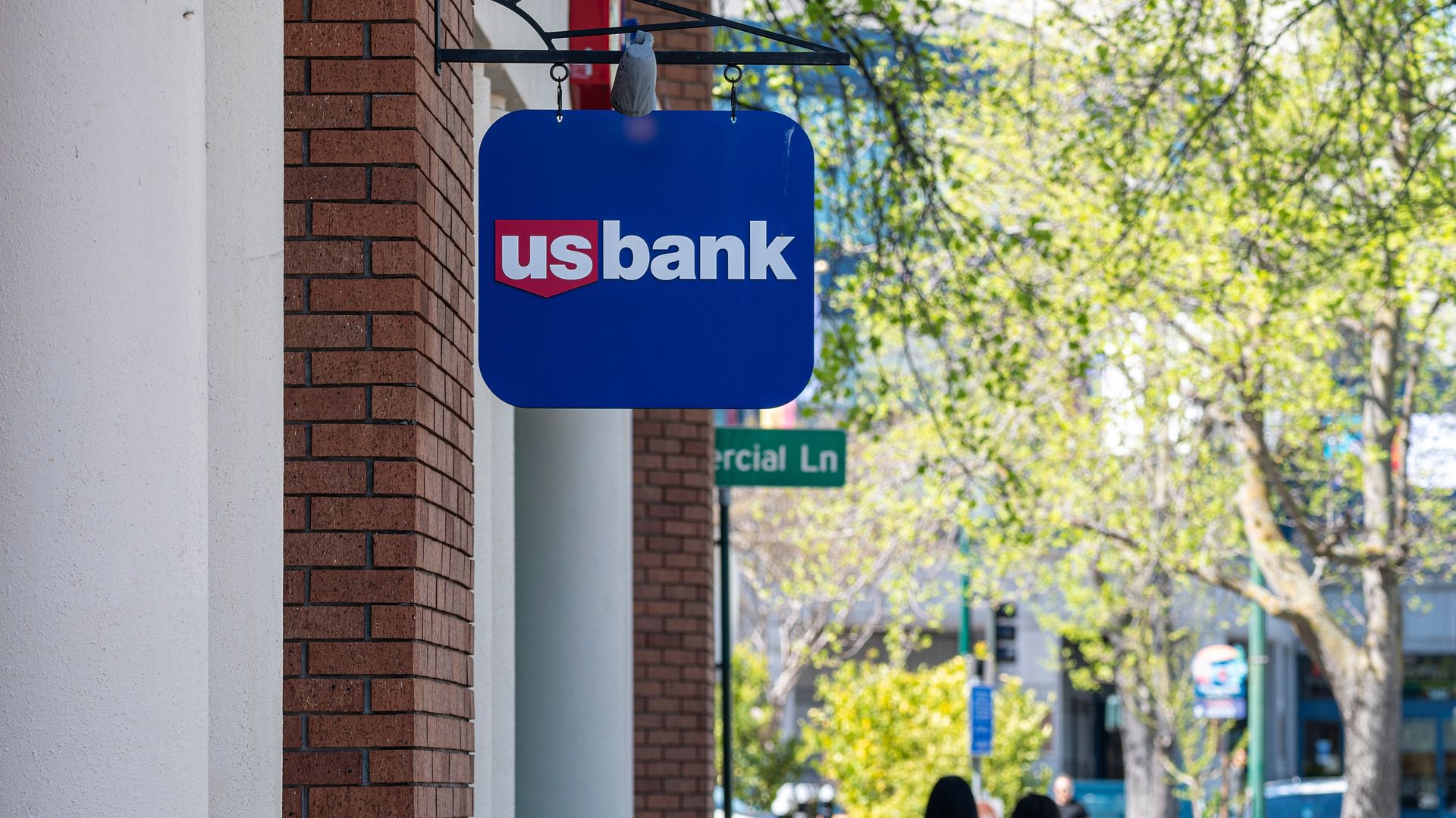 Photo of a U.S. Bank sign hanging from the side of a building as two people walk in the distance