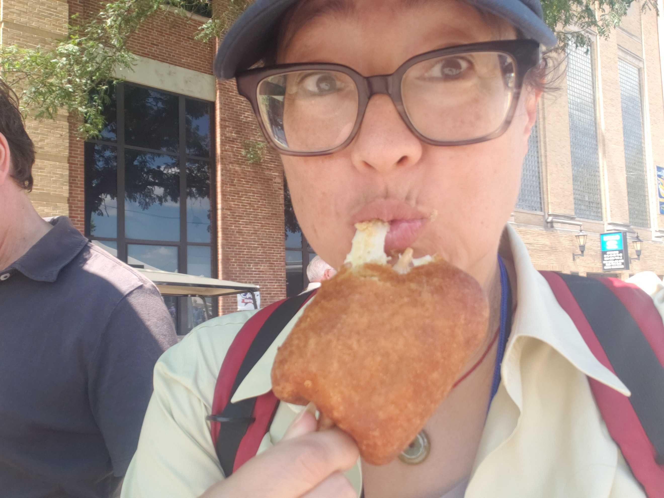Photo of a woman eating a cheesy breaded item on a stick. 