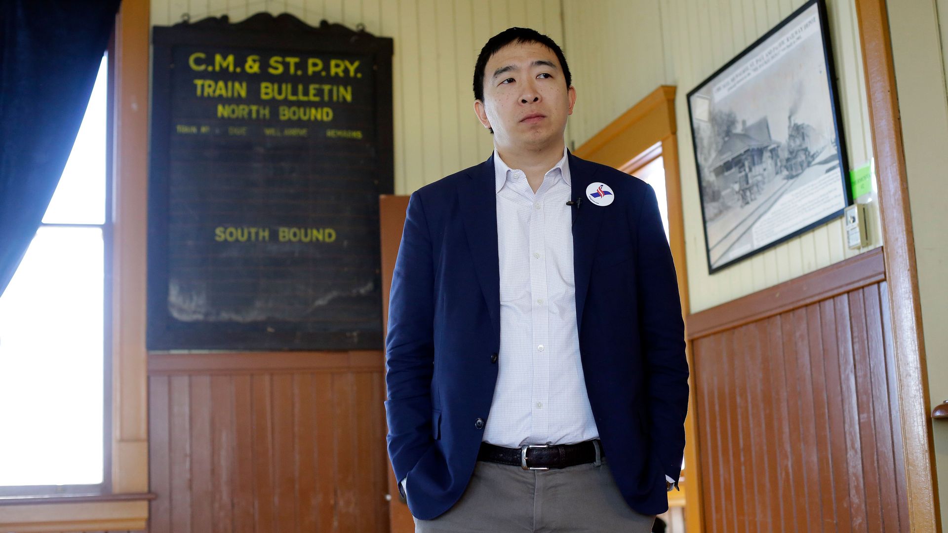 2020 candidate Andrew Yang stands in a suit jacket in front of a window.