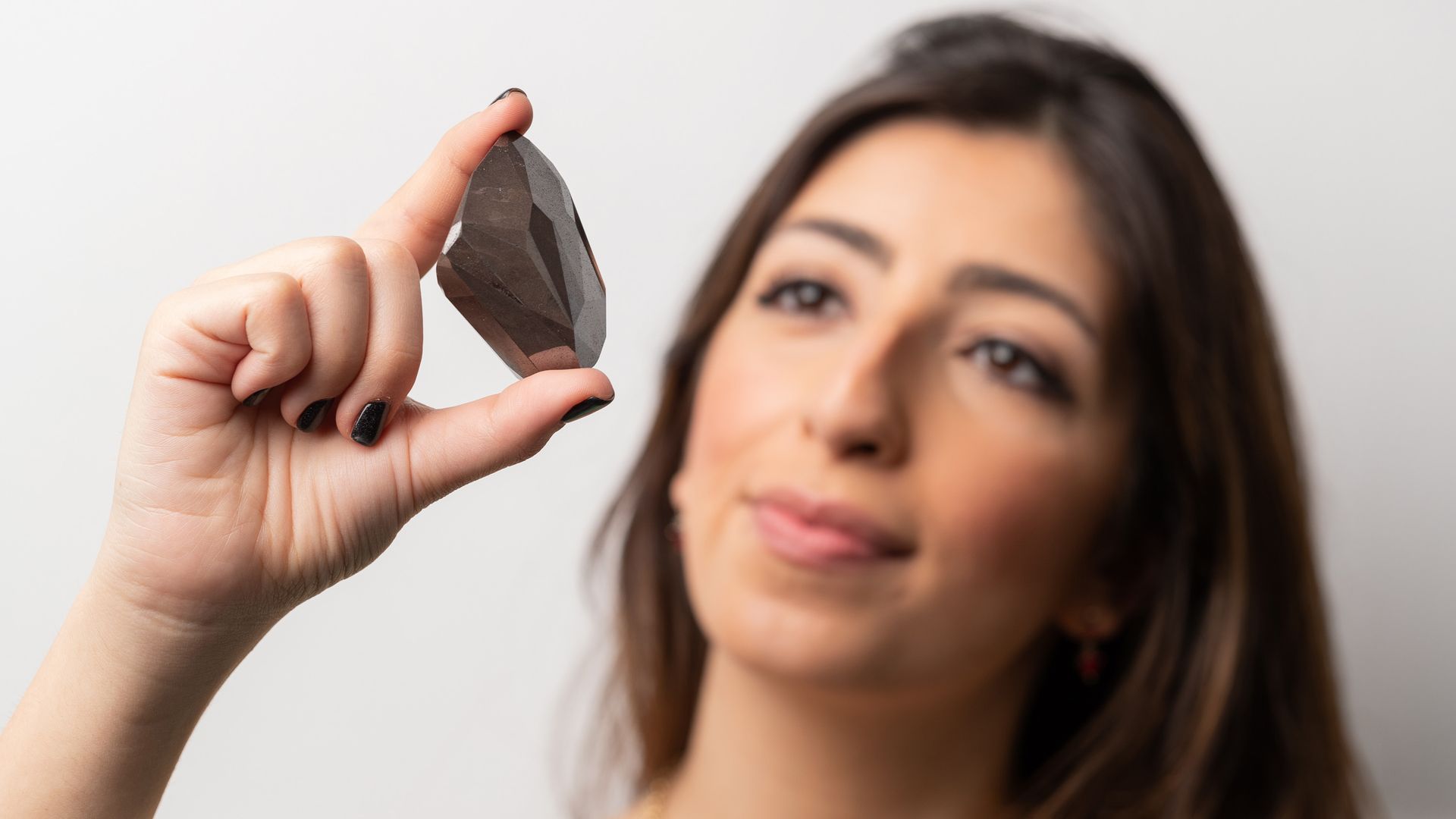 A woman holds a shiny black rock.