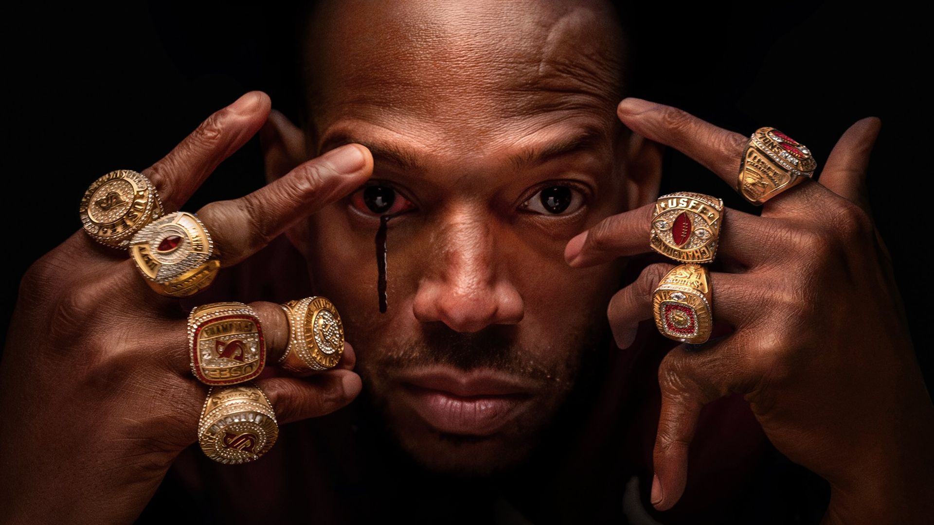 Movie poster for "HIM" showing a man with multiple gold rings on both hands holding his face, a black tear running from his left eye, with text saying "Never meet your heroes" and release date September 19.