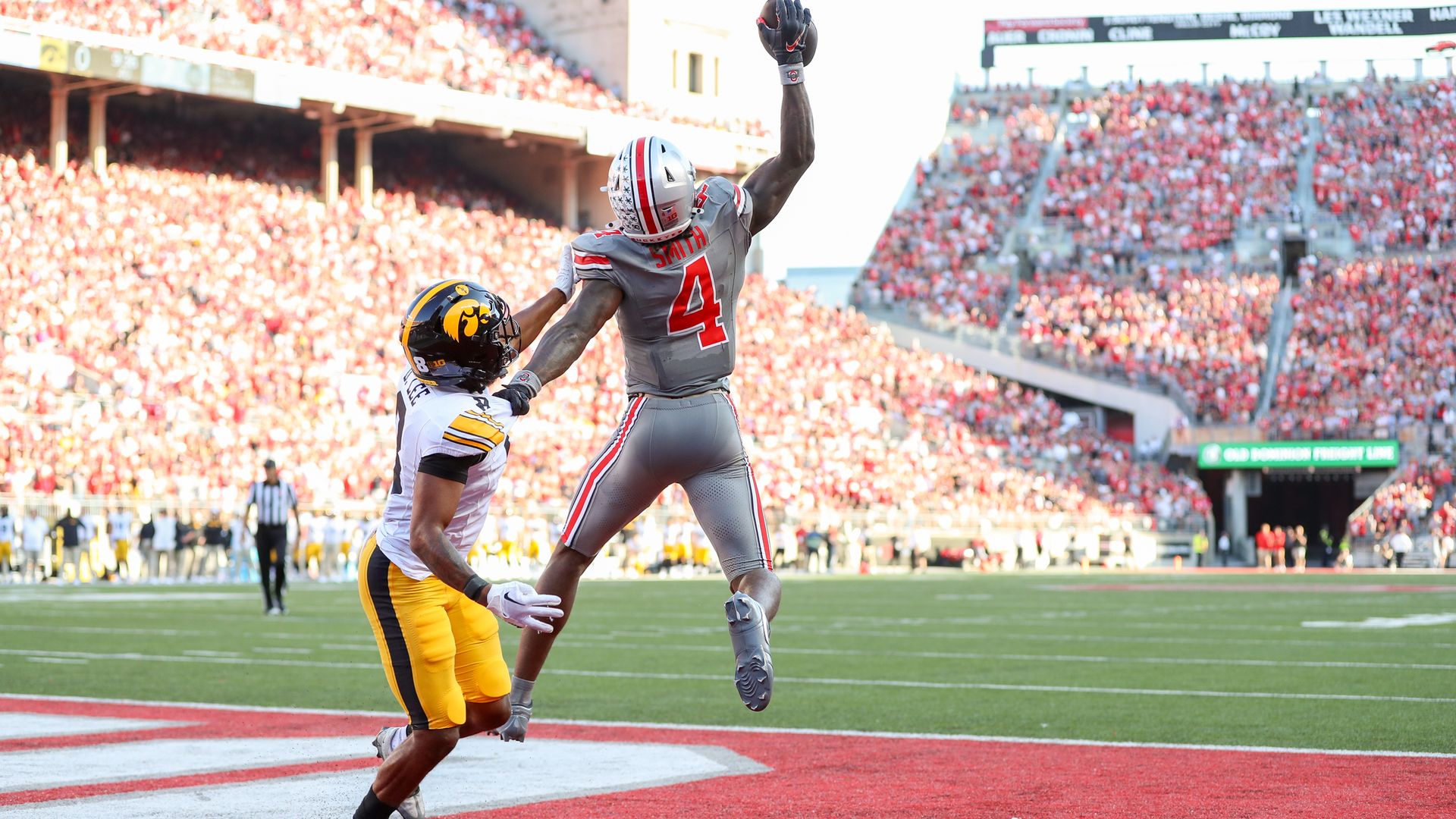 A Buckeyes receiver jumps to catch a touchdown pass while an Iowa player looks on. 